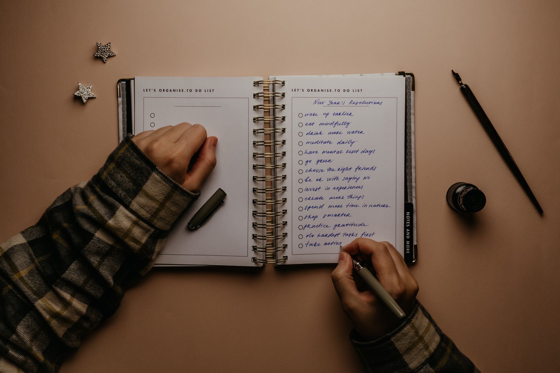 Overhead shot of a person writing New Year's resolutions in a notebook on a desk.