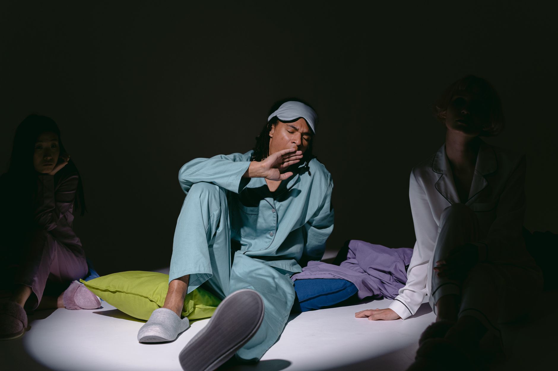 Three adults in pajamas relaxing in dim light, wearing sleep masks.
