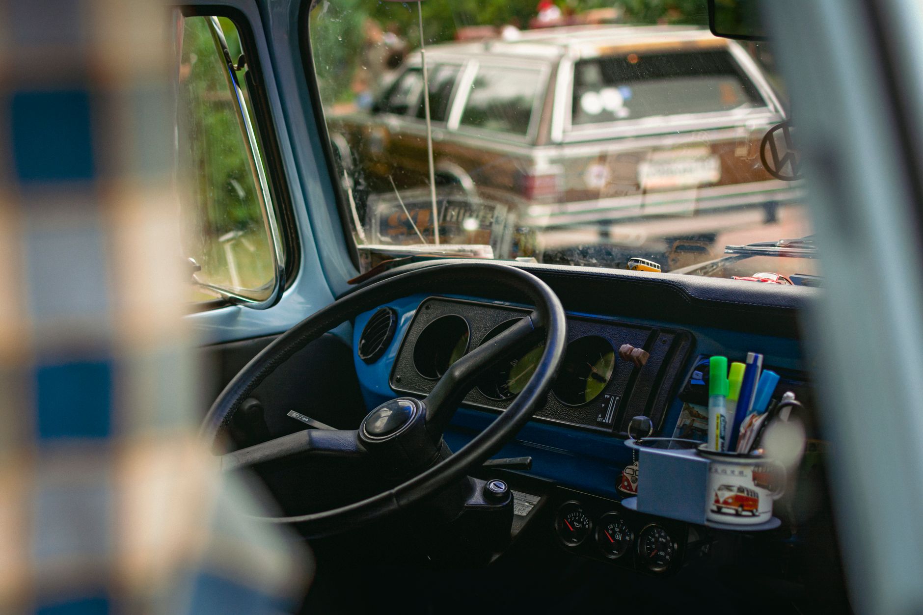 Interior view of a vintage car featuring a classic dashboard, steering wheel, and outdoor view.
