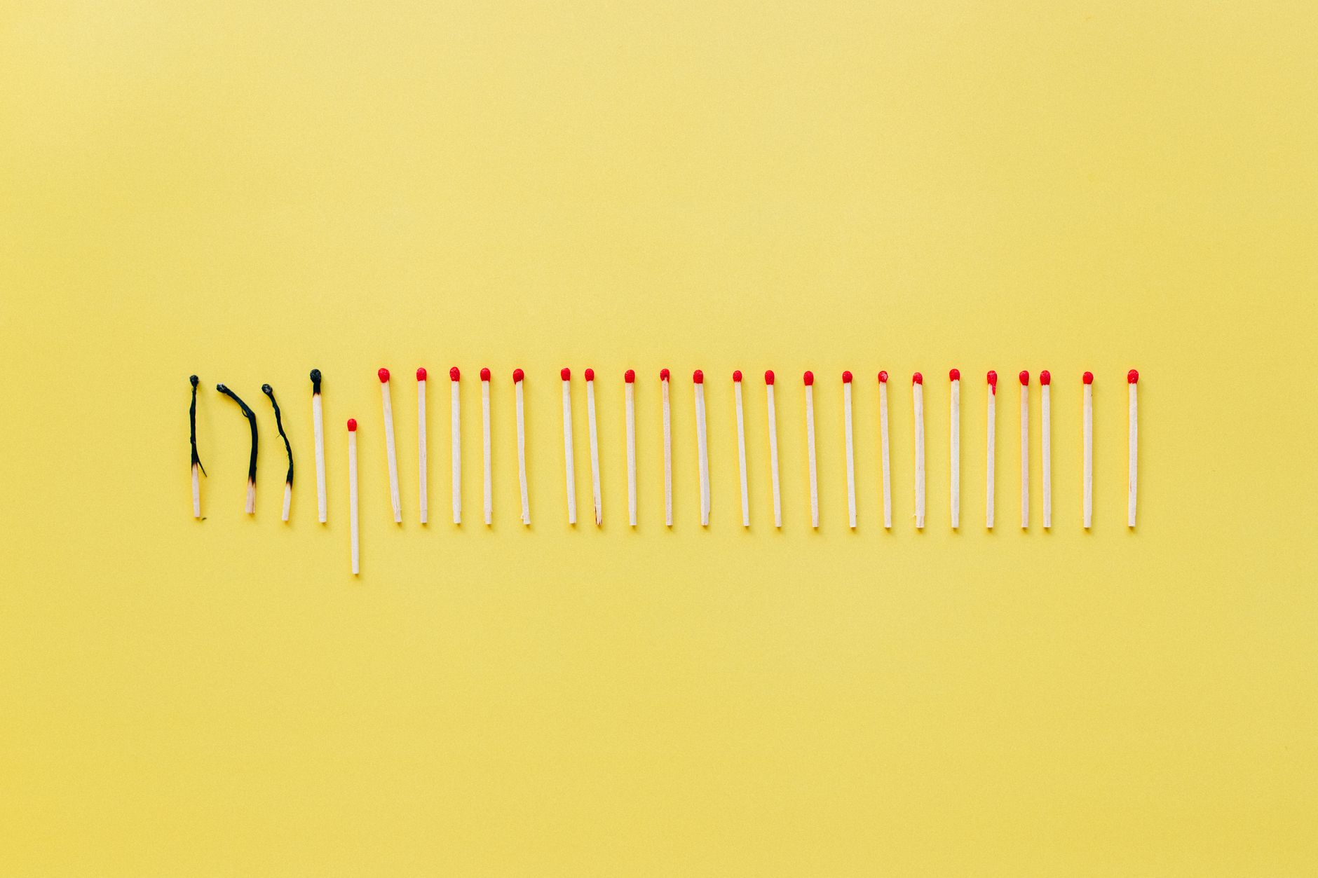 A conceptual still life photo of burnt and unlit matches on a vibrant yellow background.