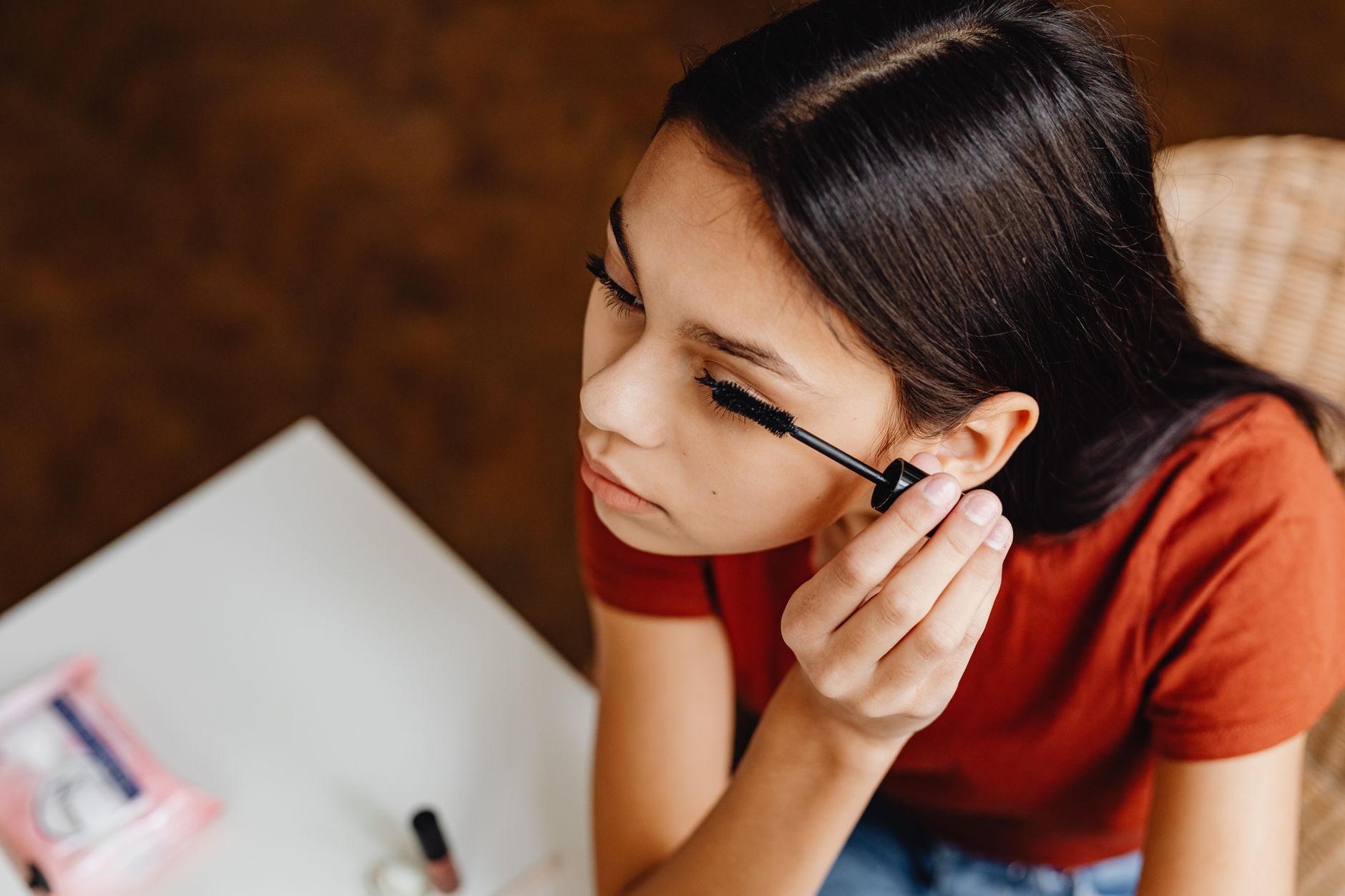 Close-up of a young woman applying mascara indoors, focusing on beauty routine.