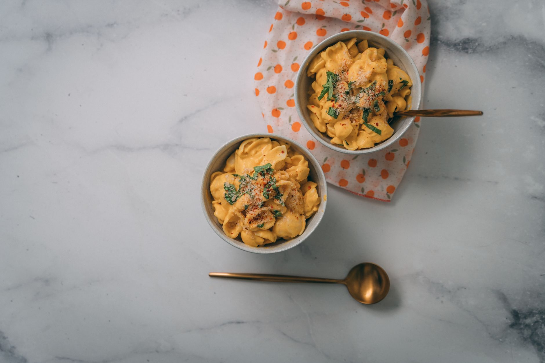 Top-down view of creamy vegan mac and cheese garnished with herbs served in bowls on a marble surface.