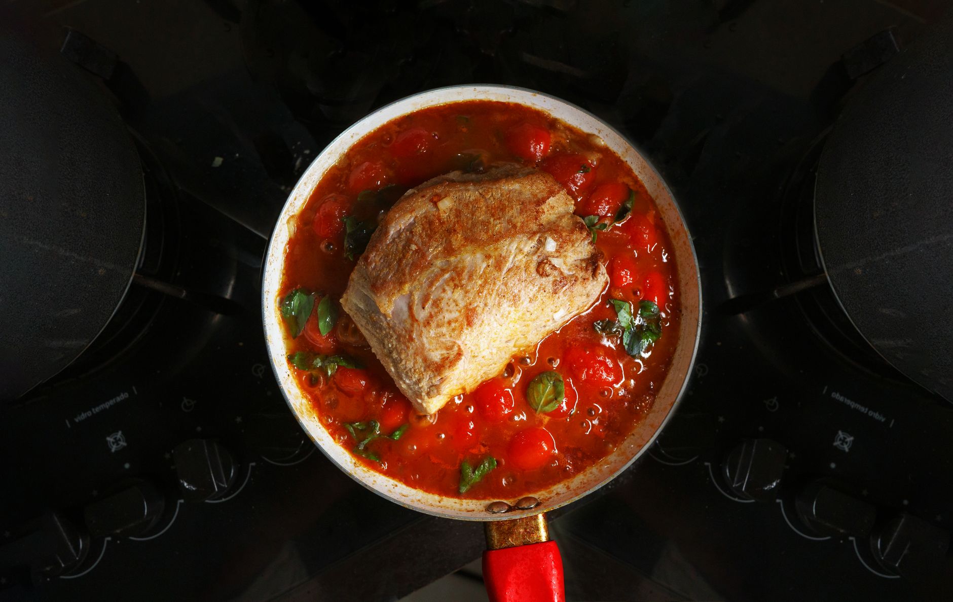 A savory roast beef cooked in rich tomato sauce with herbs, atop a stovetop.