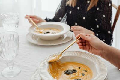 A close-up of hands enjoying creamy pumpkin soup at an elegant dining table setting.