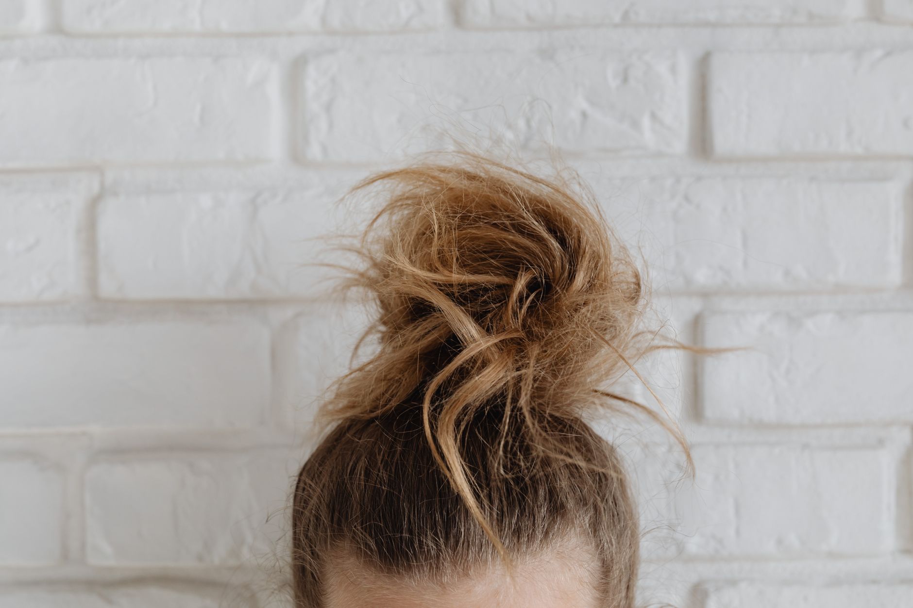 Close-up of a casual messy bun hairstyle in front of a textured white brick wall.