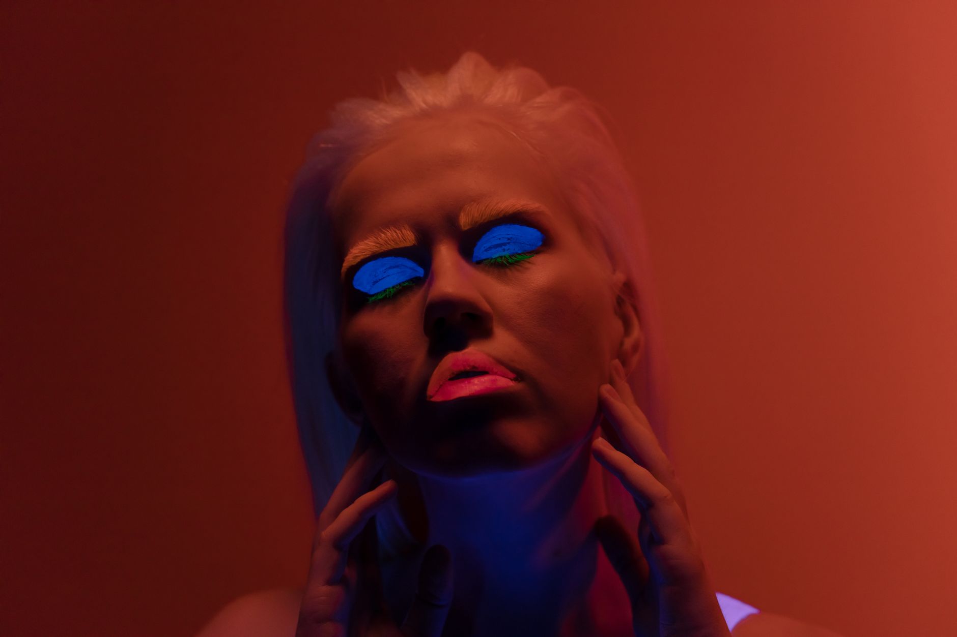 A striking portrait of a woman with neon makeup against an orange backdrop, creating a luminous and conceptual aesthetic.