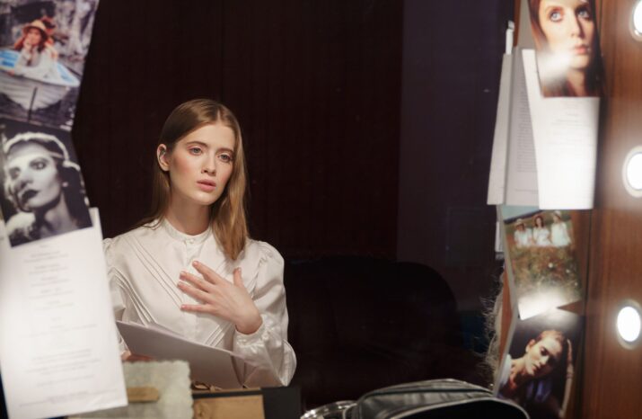 A contemplative actress in a dressing room, reading a script in front of an illuminated mirror.