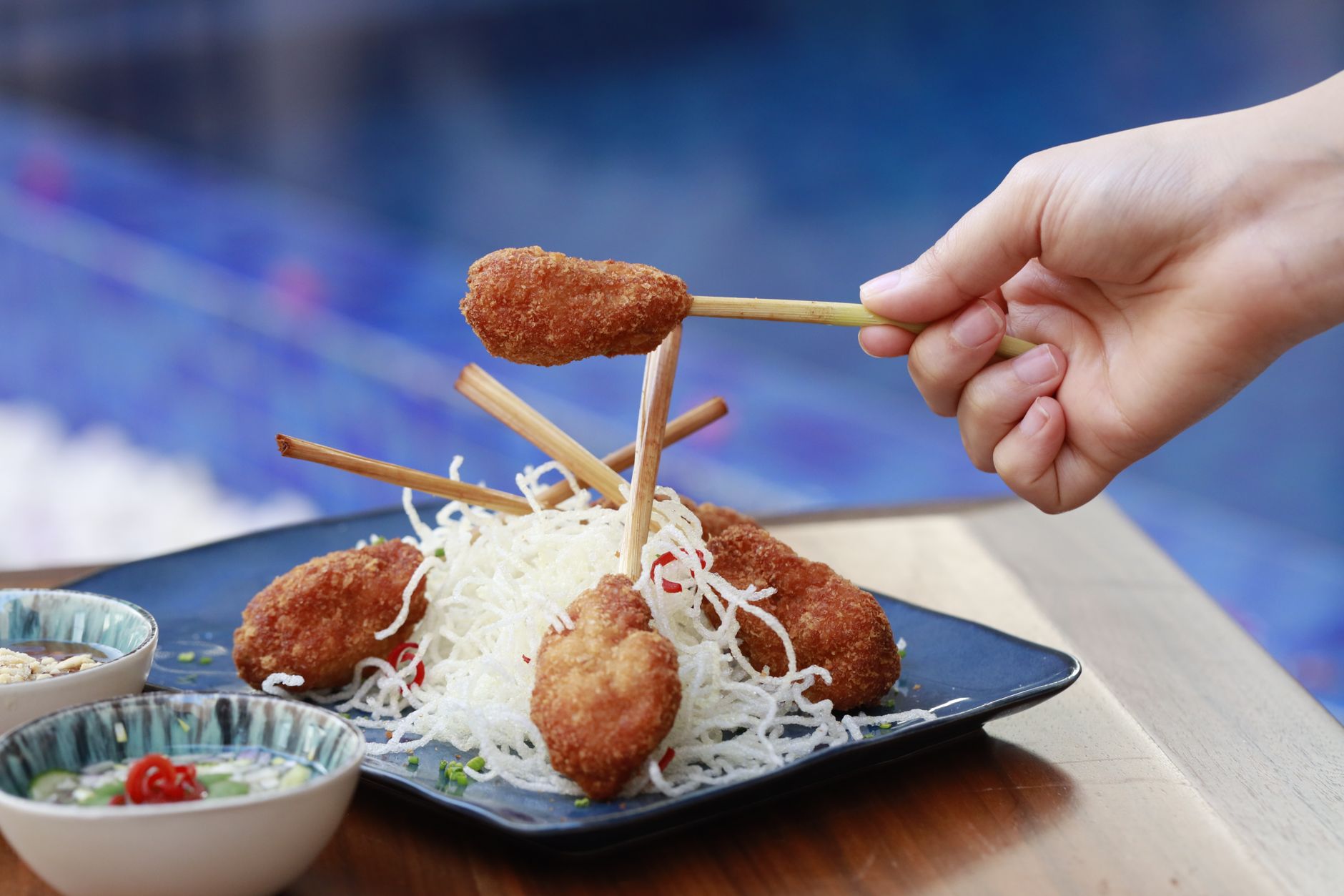 A close-up view of Asian skewered meat on a plate with human hand interaction.