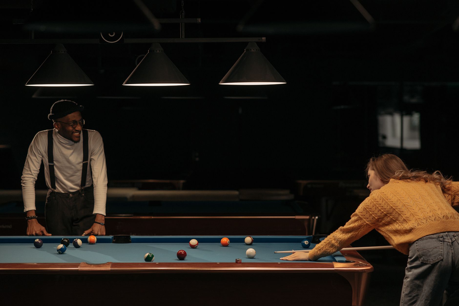 A woman takes a shot at billiards while a man watches, creating a relaxed indoor atmosphere.