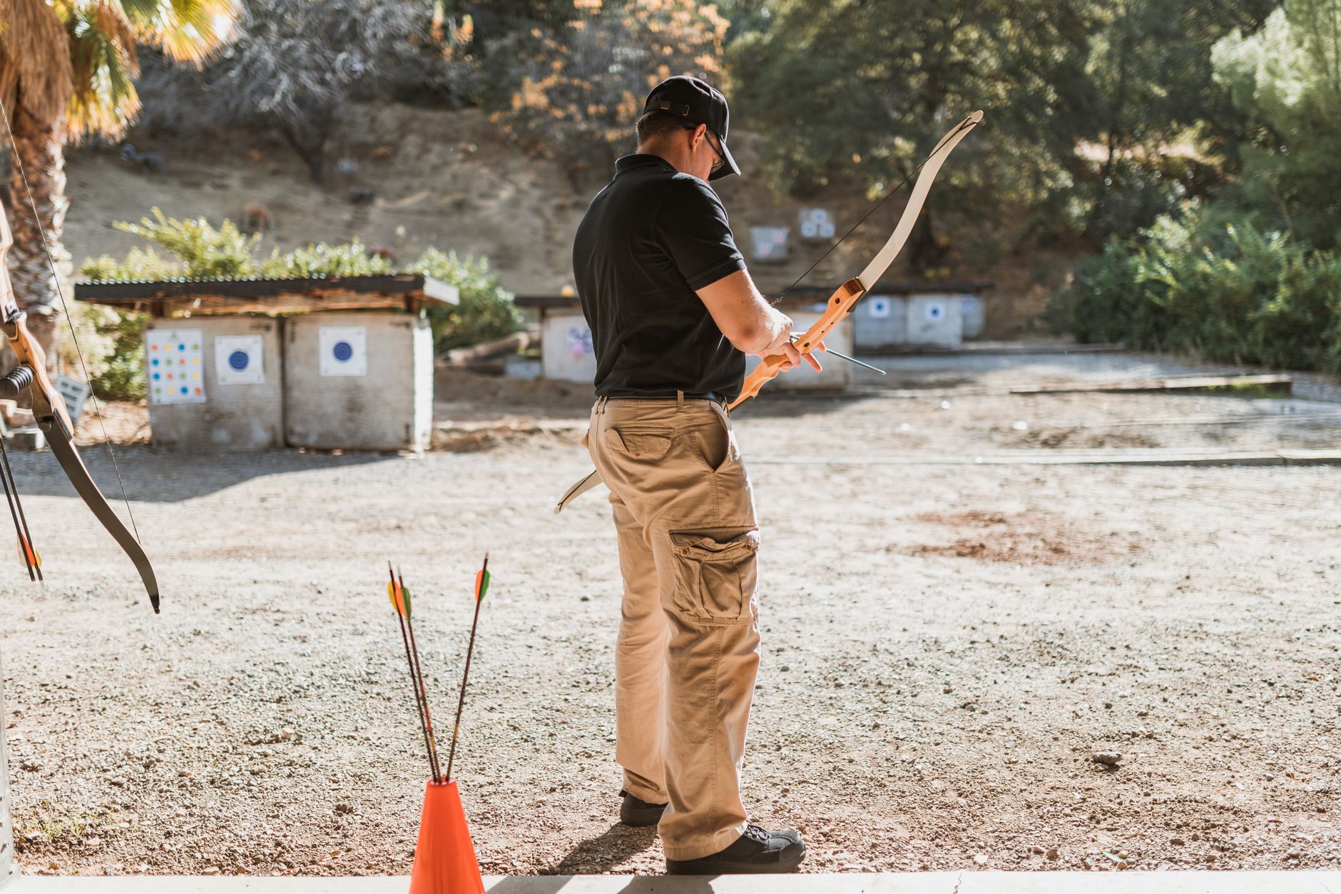An adult male practicing archery outdoors with a recurve bow, focused on target practice.