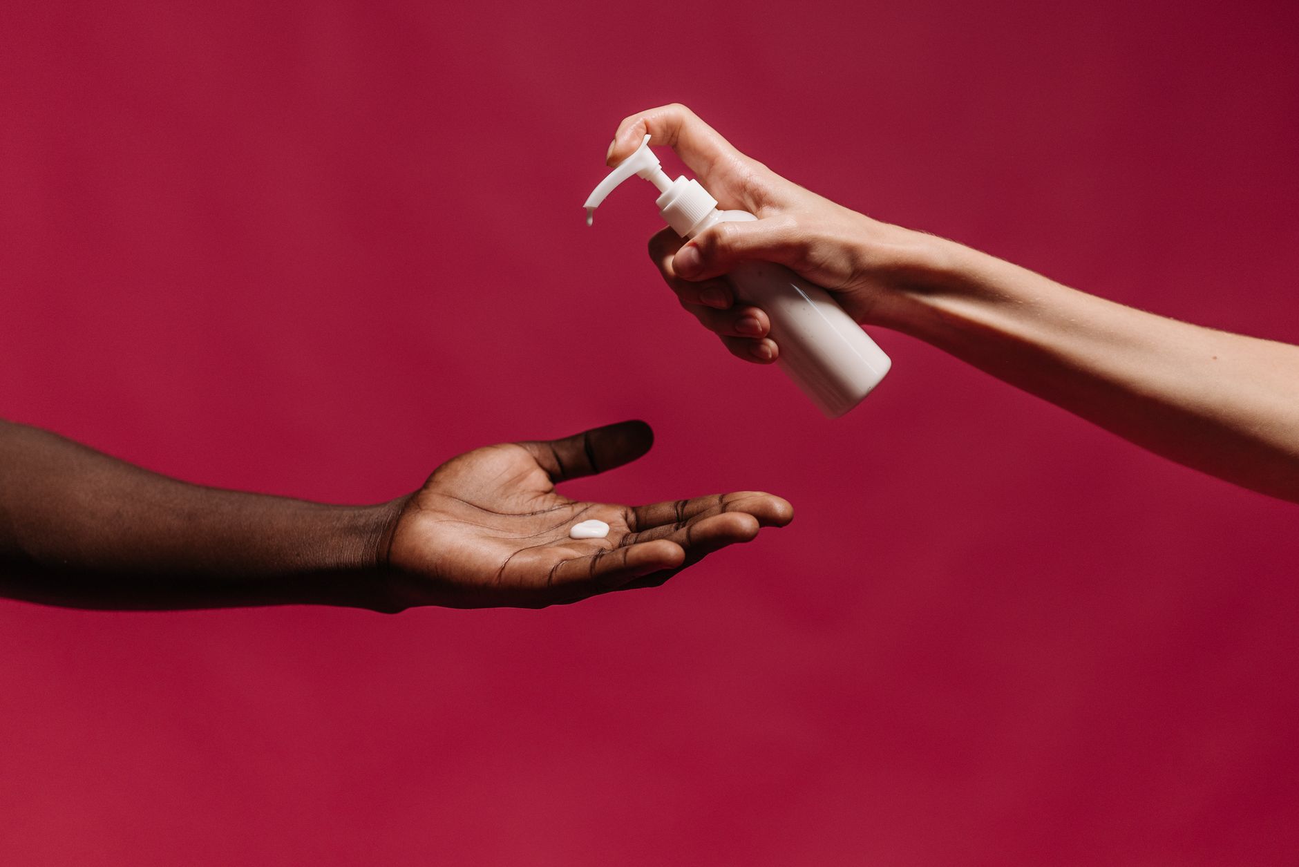 Close-up of hands applying lotion from a pump bottle against a vibrant red background.