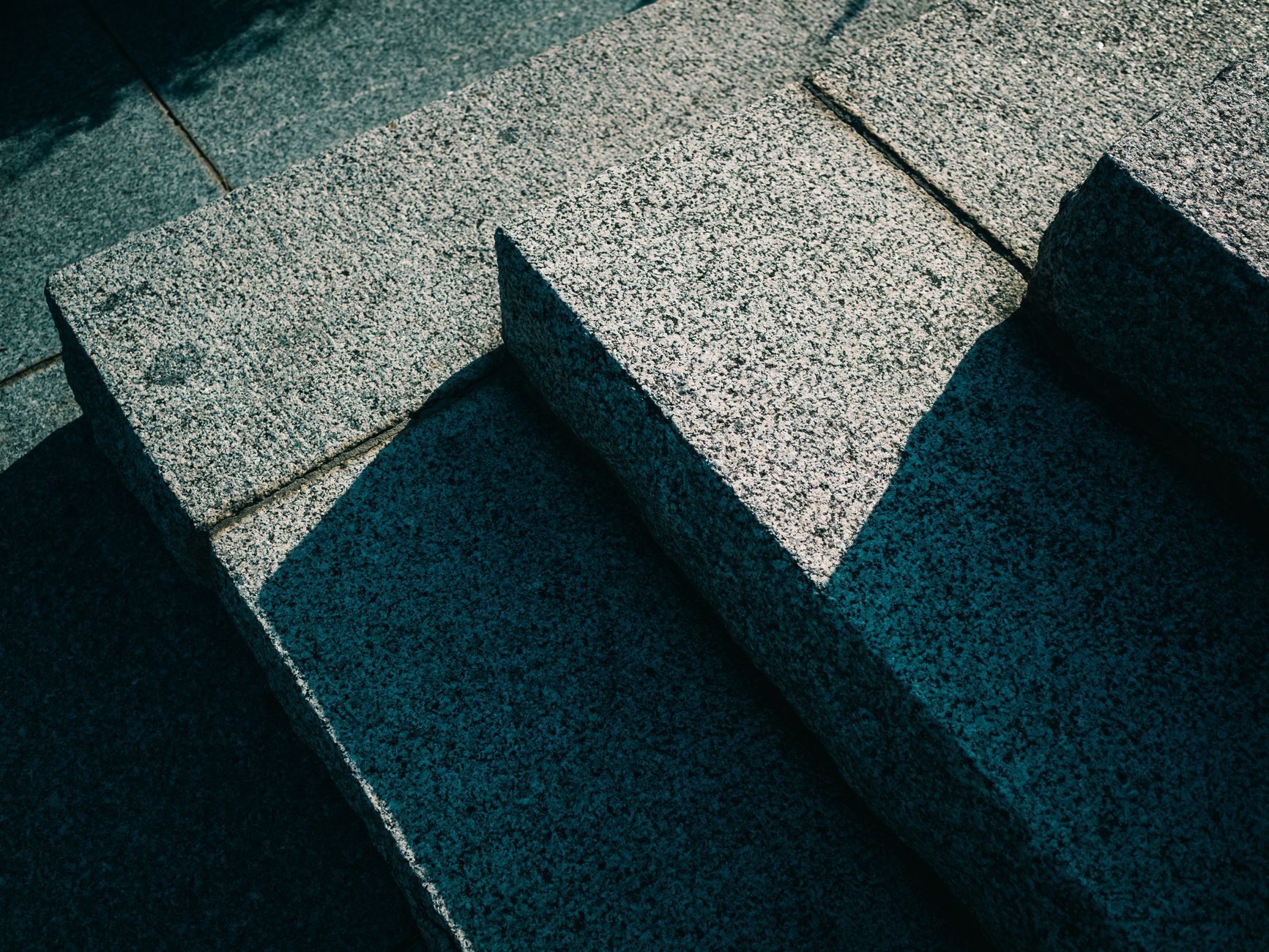 Dramatic shadows create abstract patterns on stone steps in a city setting, showcasing urban textures.