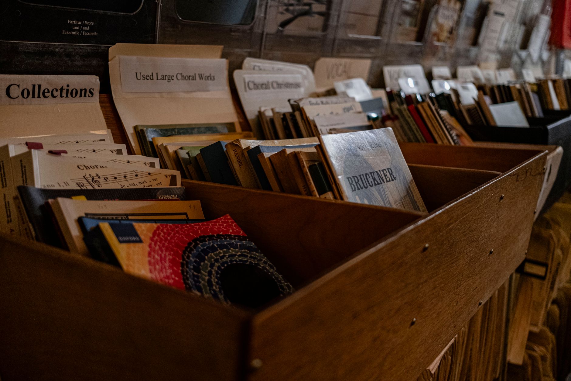 Close-up view of assorted sheet music stored in a wooden file drawer in a music store.