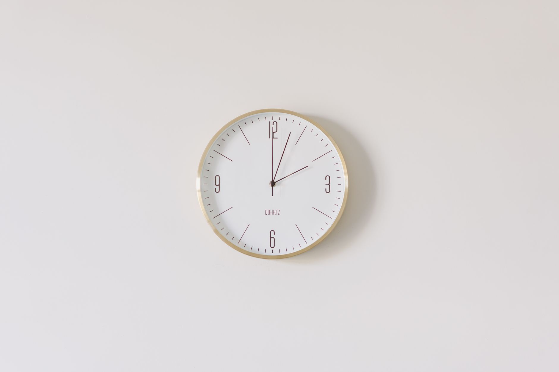 Minimalist round wall clock with gold rim and white face on a white wall.
