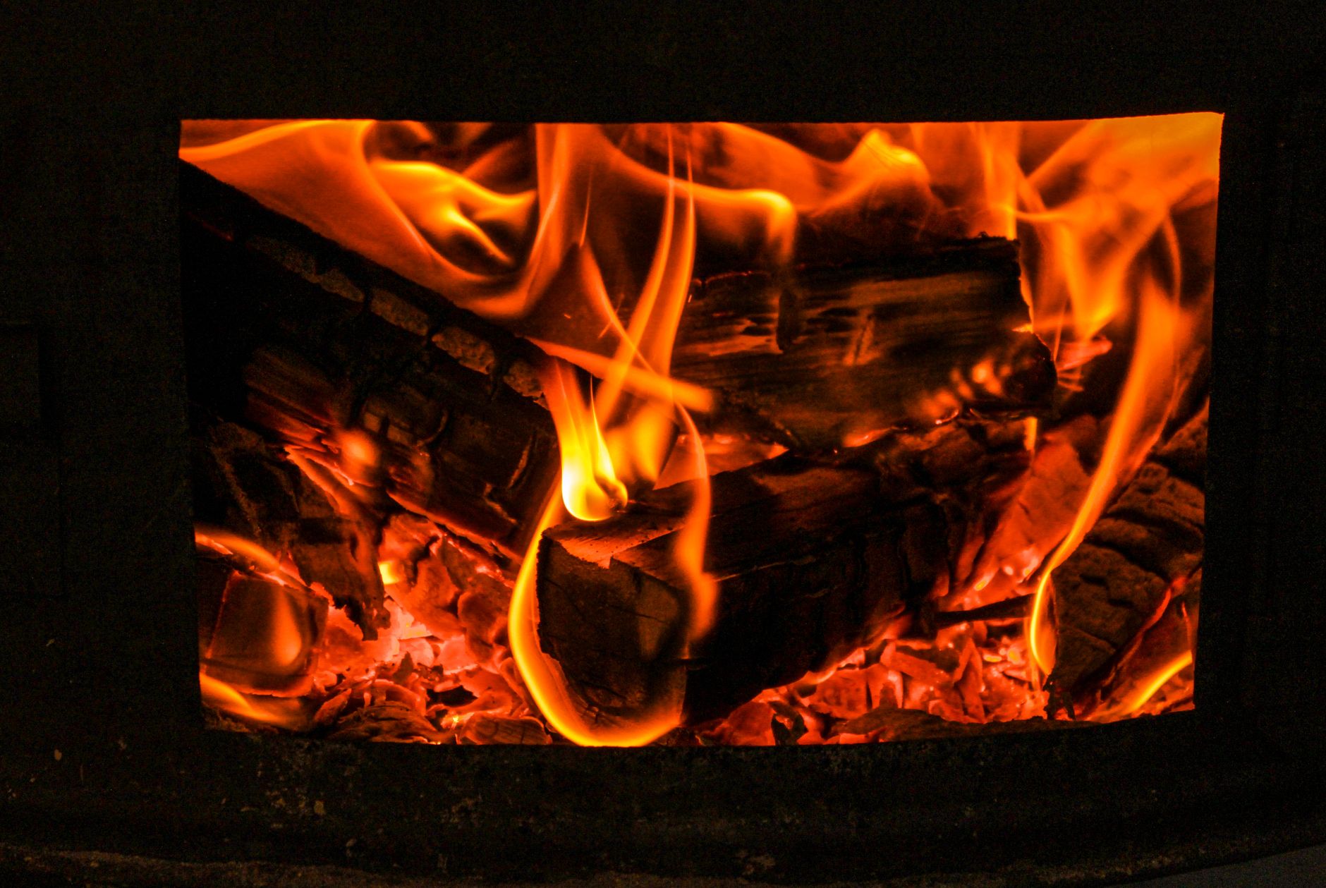 Close macro shot of vibrant orange flames engulfing firewood in a stove.