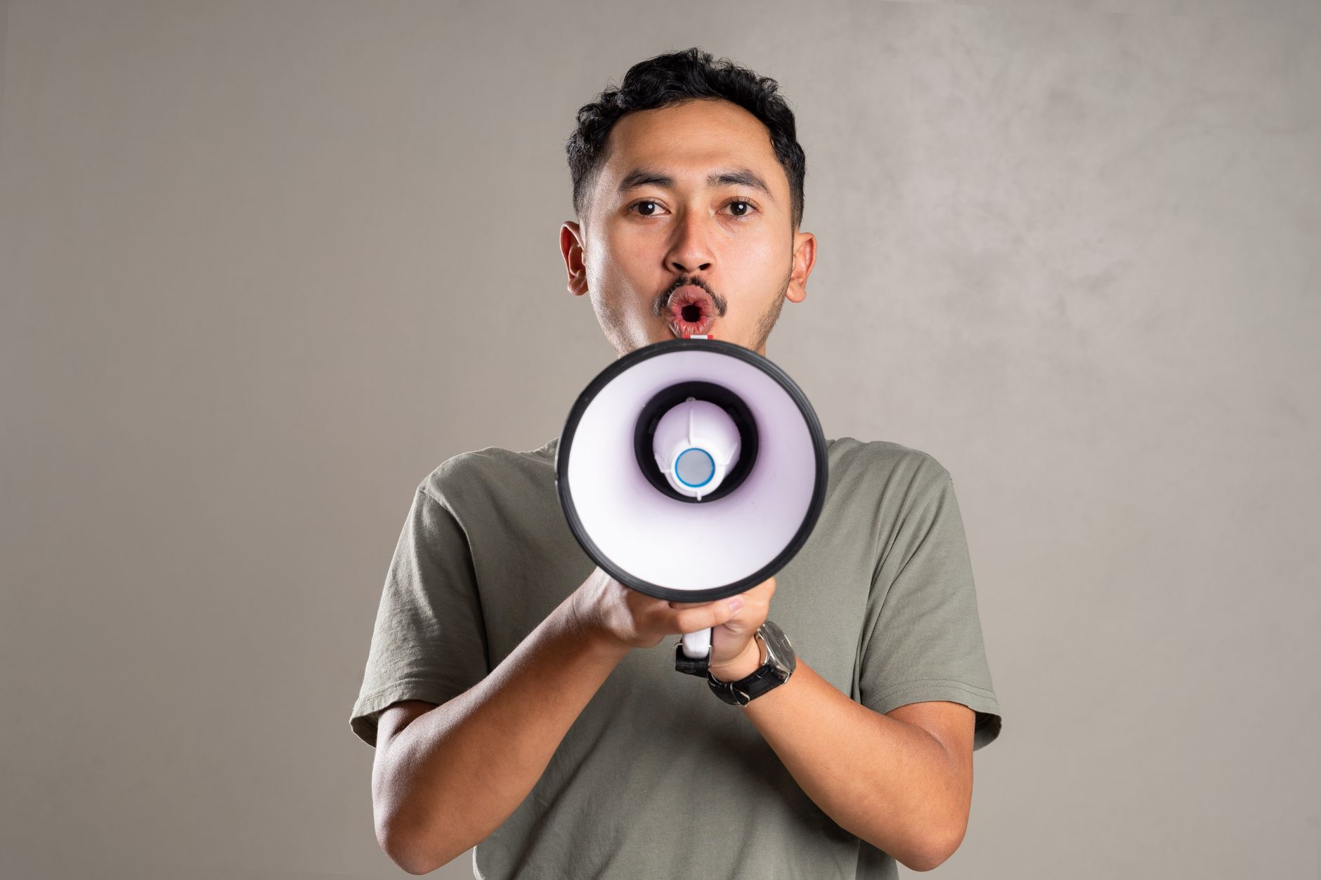 Young man holding a megaphone shouting in a studio setting. Expression of communication.