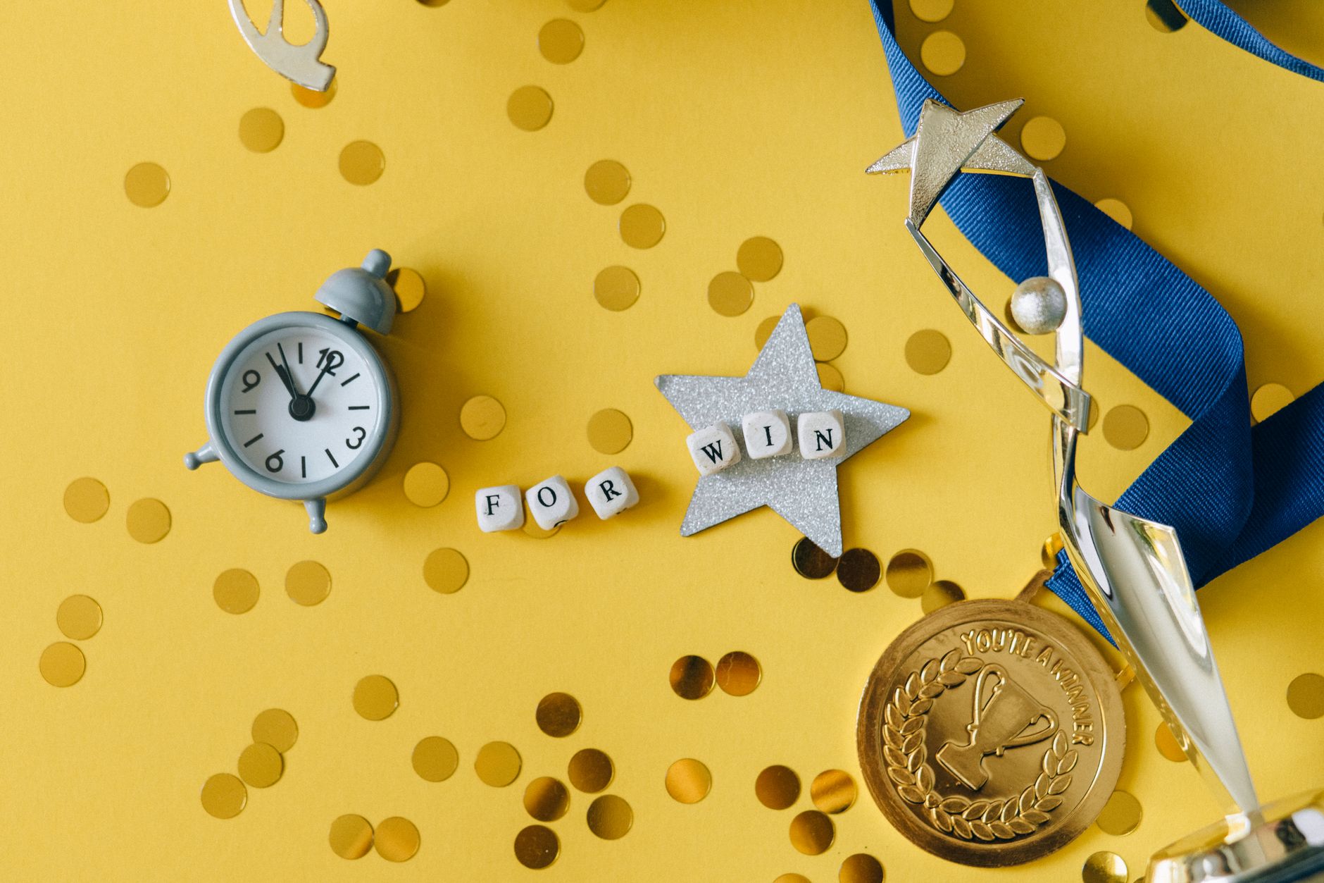 Conceptual flat lay of a trophy, medal, and clock with 'FOR WIN' letters, symbolizing victory and achievement.