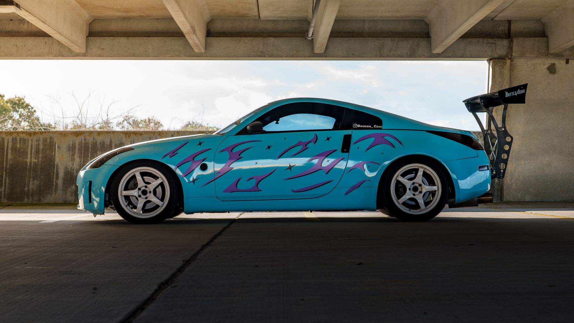 Side view of a blue sports car with custom paint under a concrete structure.