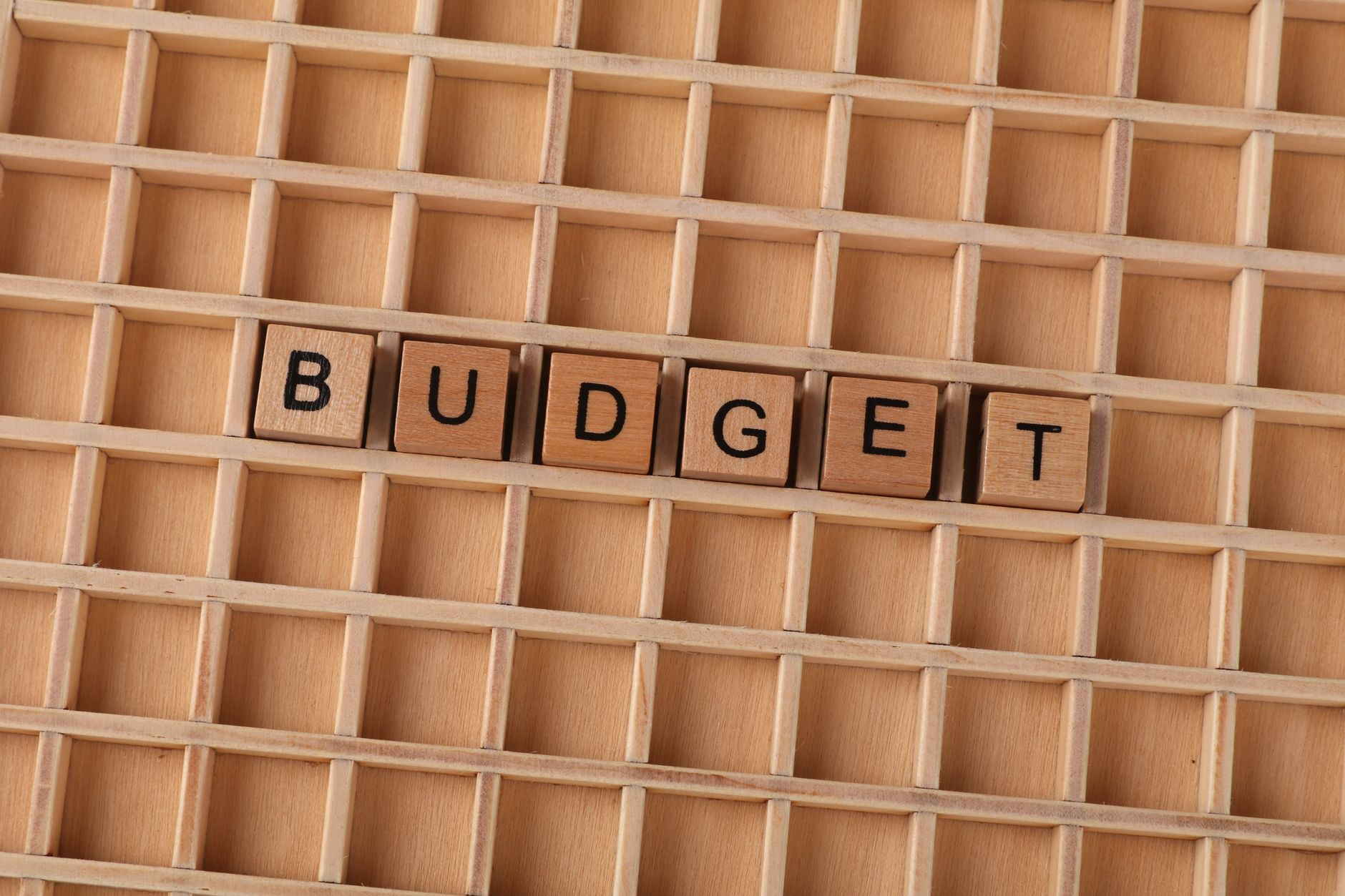Wooden Scrabble tiles spelling 'budget' on a textured wooden grid, symbolizing financial planning.