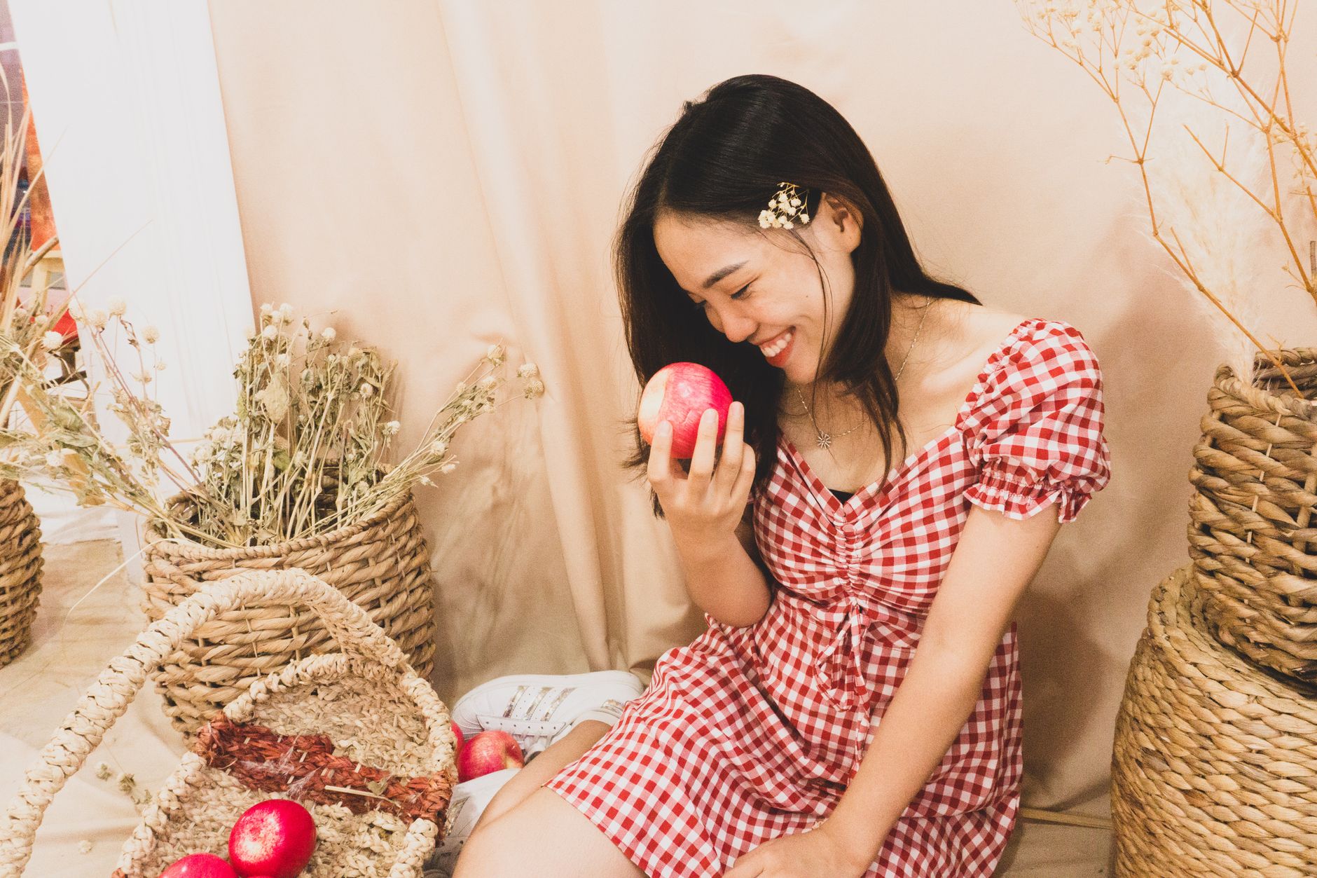 A joyful woman with a red apple sits among baskets, exuding warmth and charm.