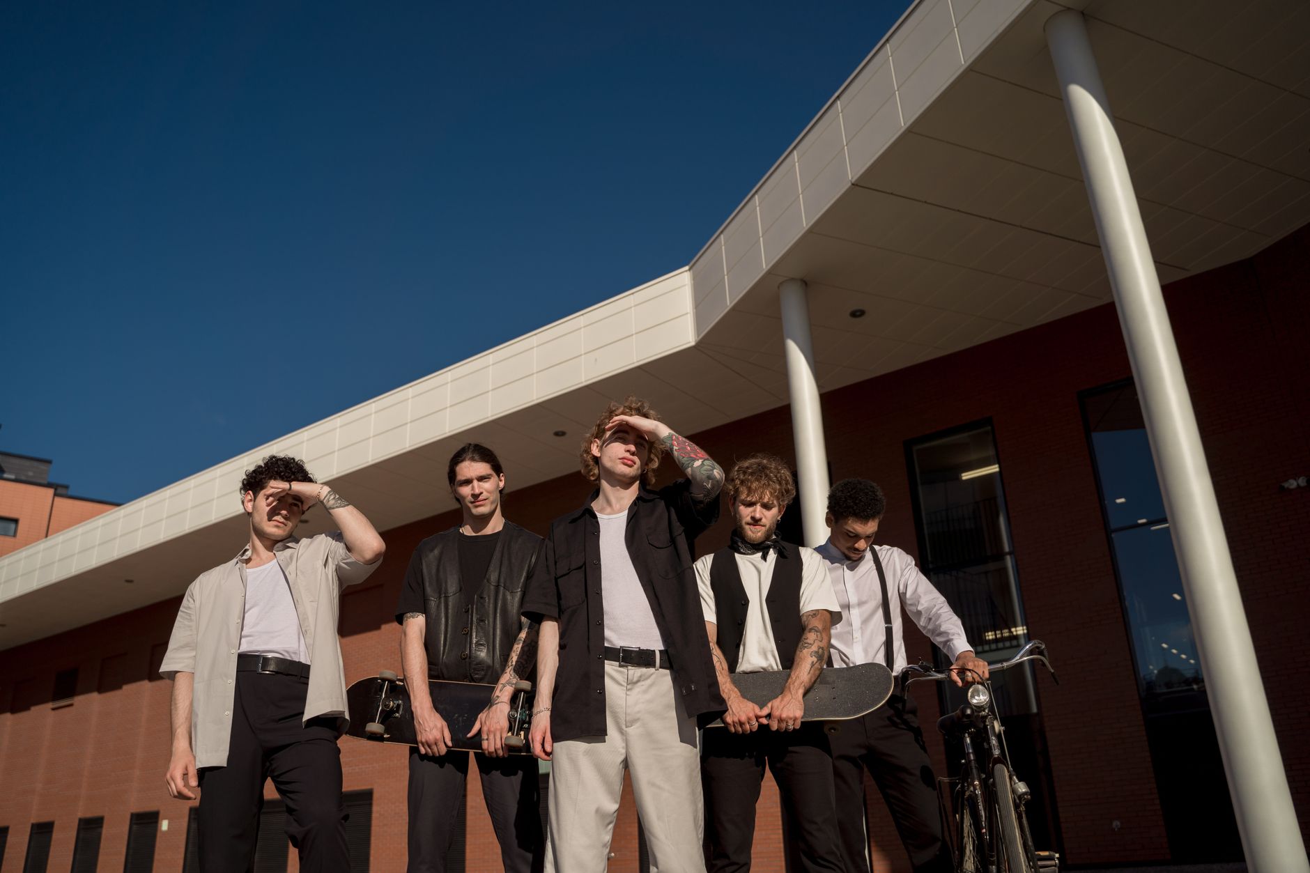 A group of young men posing with skateboards and a bicycle outside a modern building.
