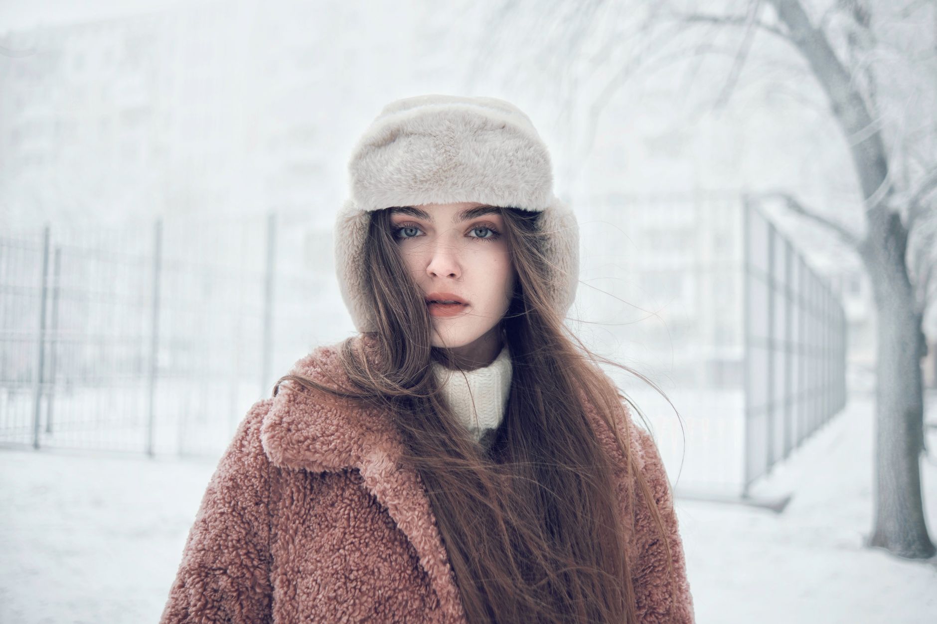Stylish winter fashion portrait of a woman in fur hat and coat, standing in snowy outdoor setting.