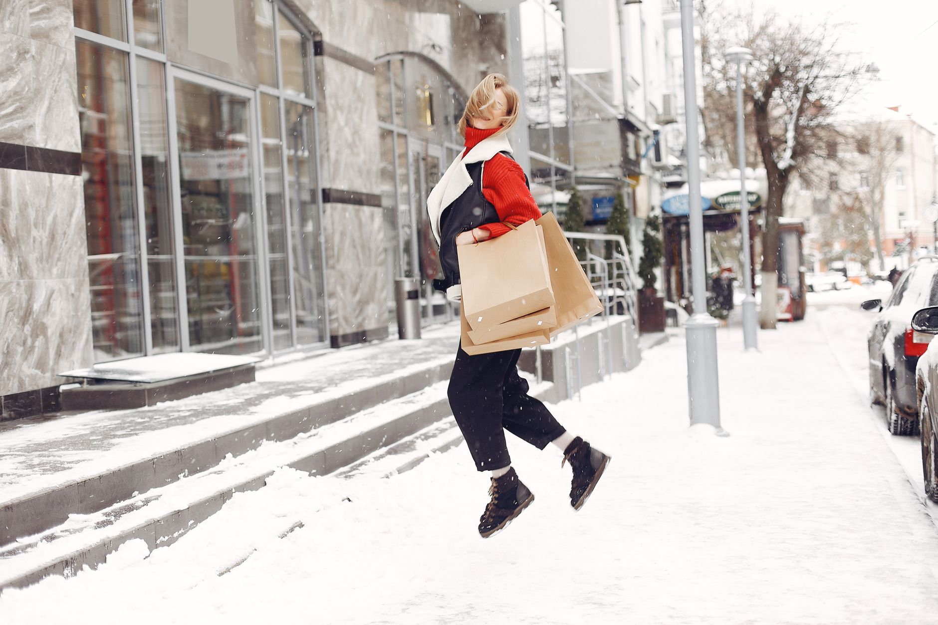 A happy woman jumps with shopping bags in a snowy city street during winter.