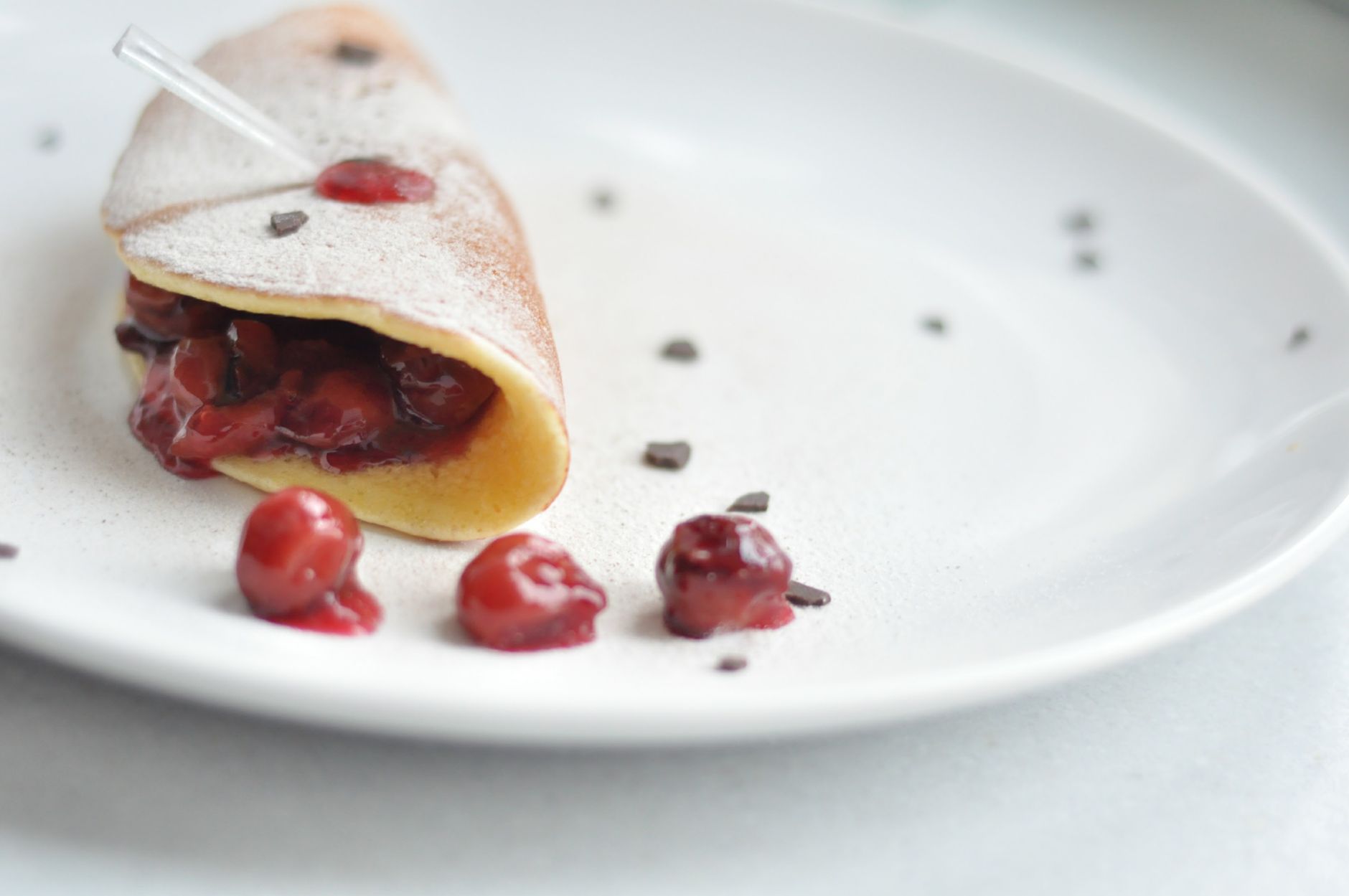 Delicious crepe filled with cherry compote, dusted with powdered sugar on a white plate.