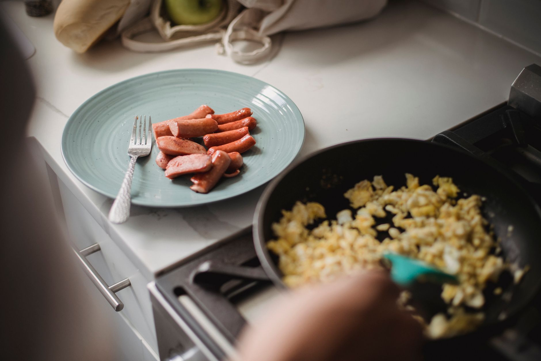 High angle view of breakfast preparation with sausages and scrambled eggs in a kitchen setting.
