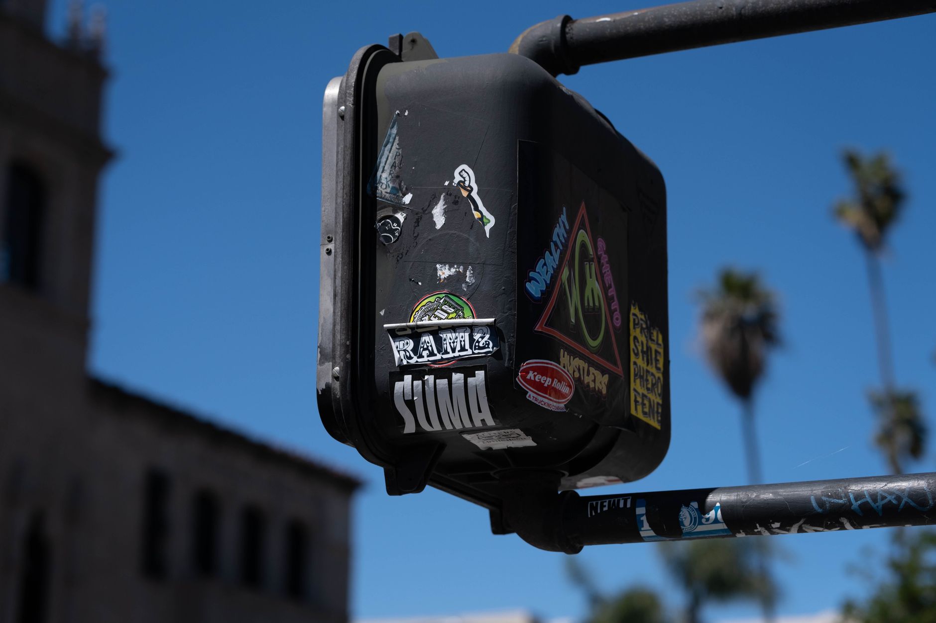 Urban scene with stickers on a traffic light against a clear blue sky in Los Angeles.