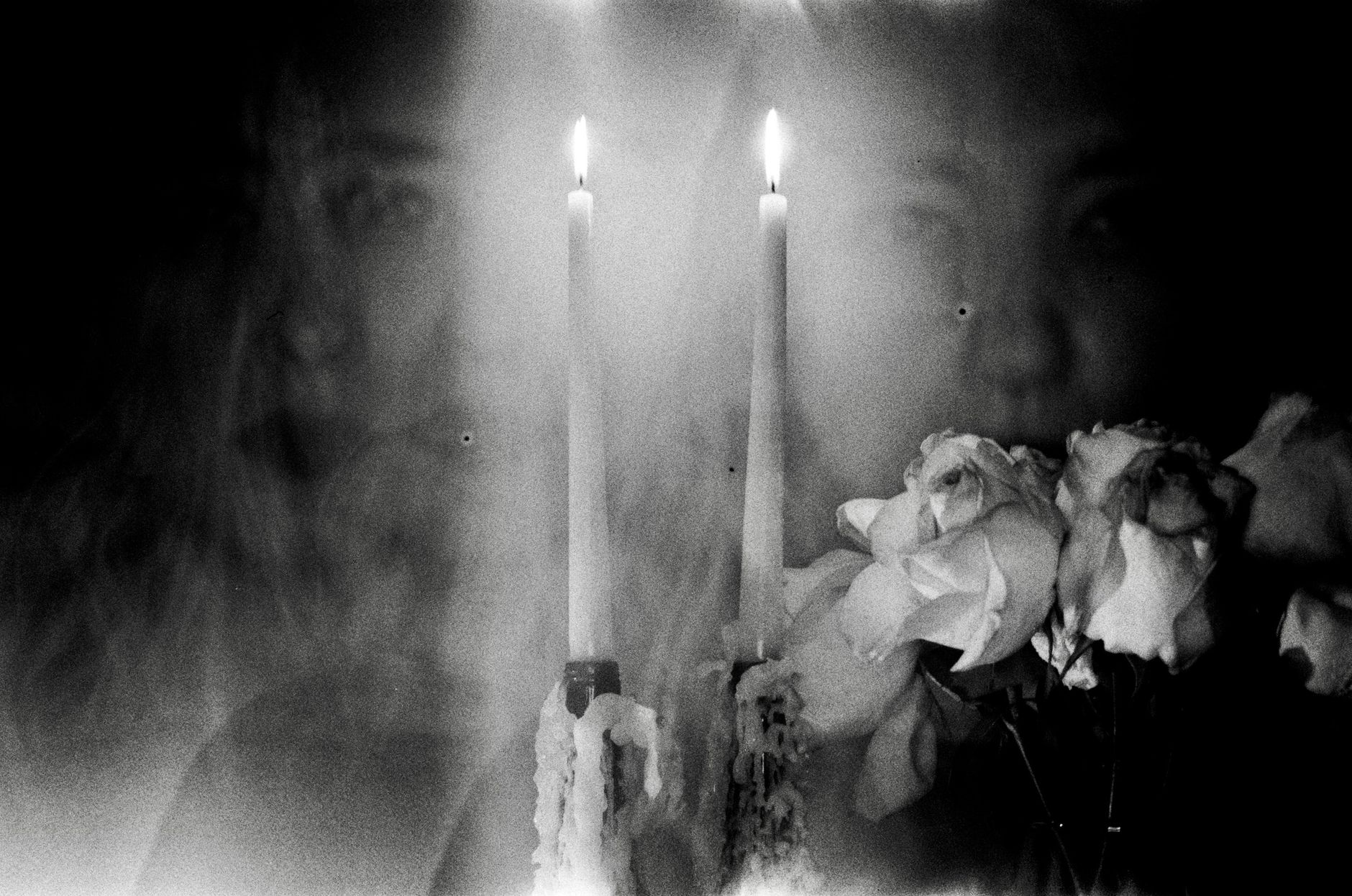 Ethereal black and white portrait of a woman with candles and roses, conveying mystery.