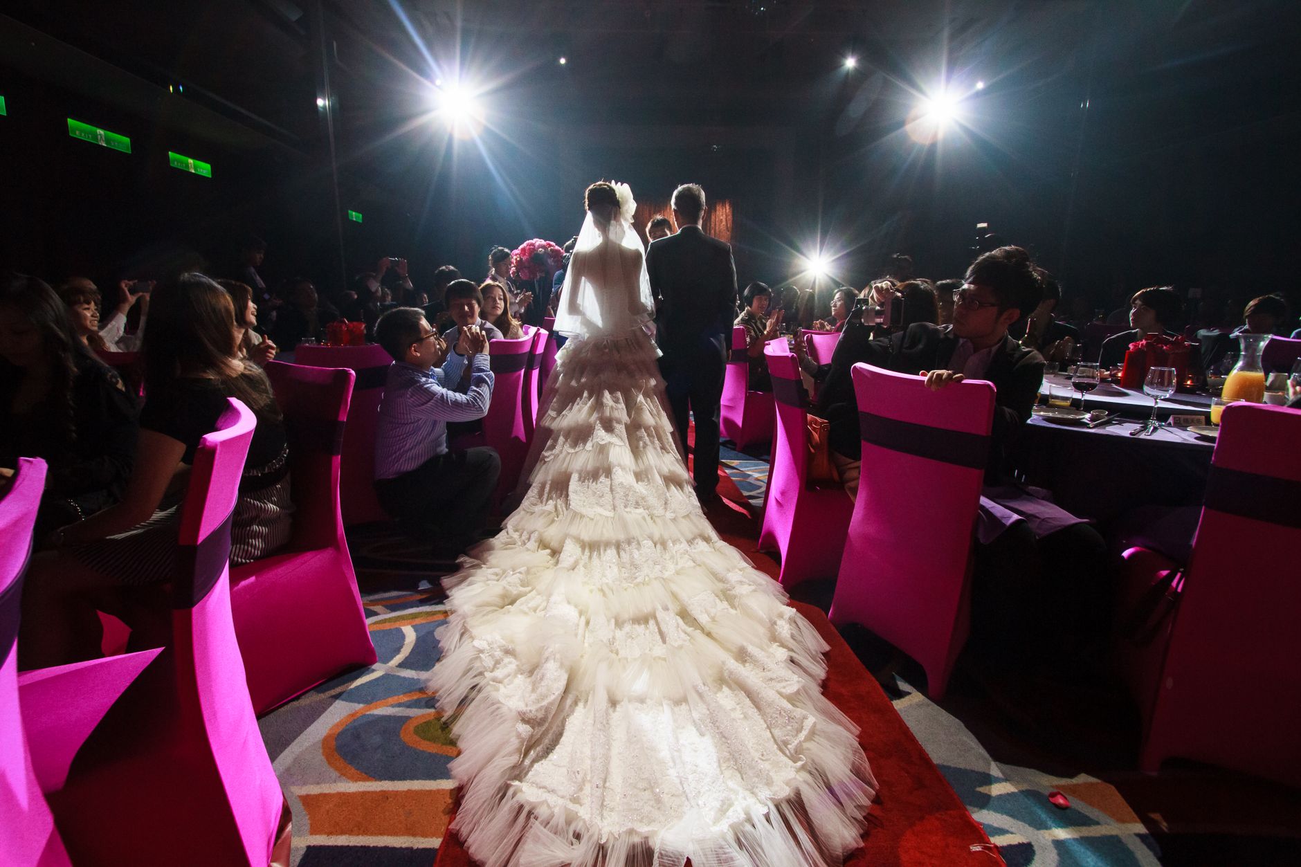 A bride and groom walk down the aisle at an elegant indoor wedding reception.