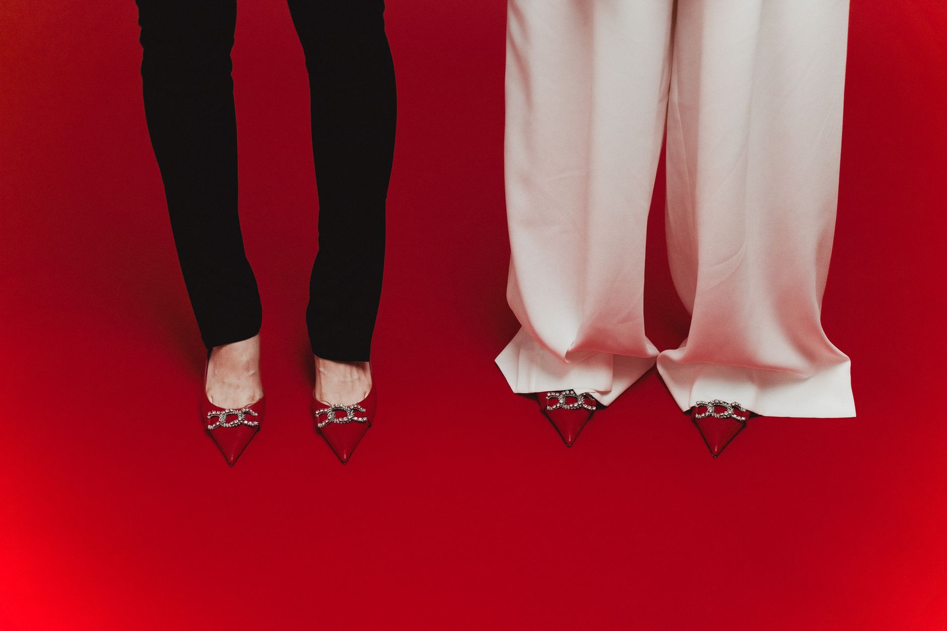 Elegant red shoes with crystal designs paired with black and white pants on red surface.