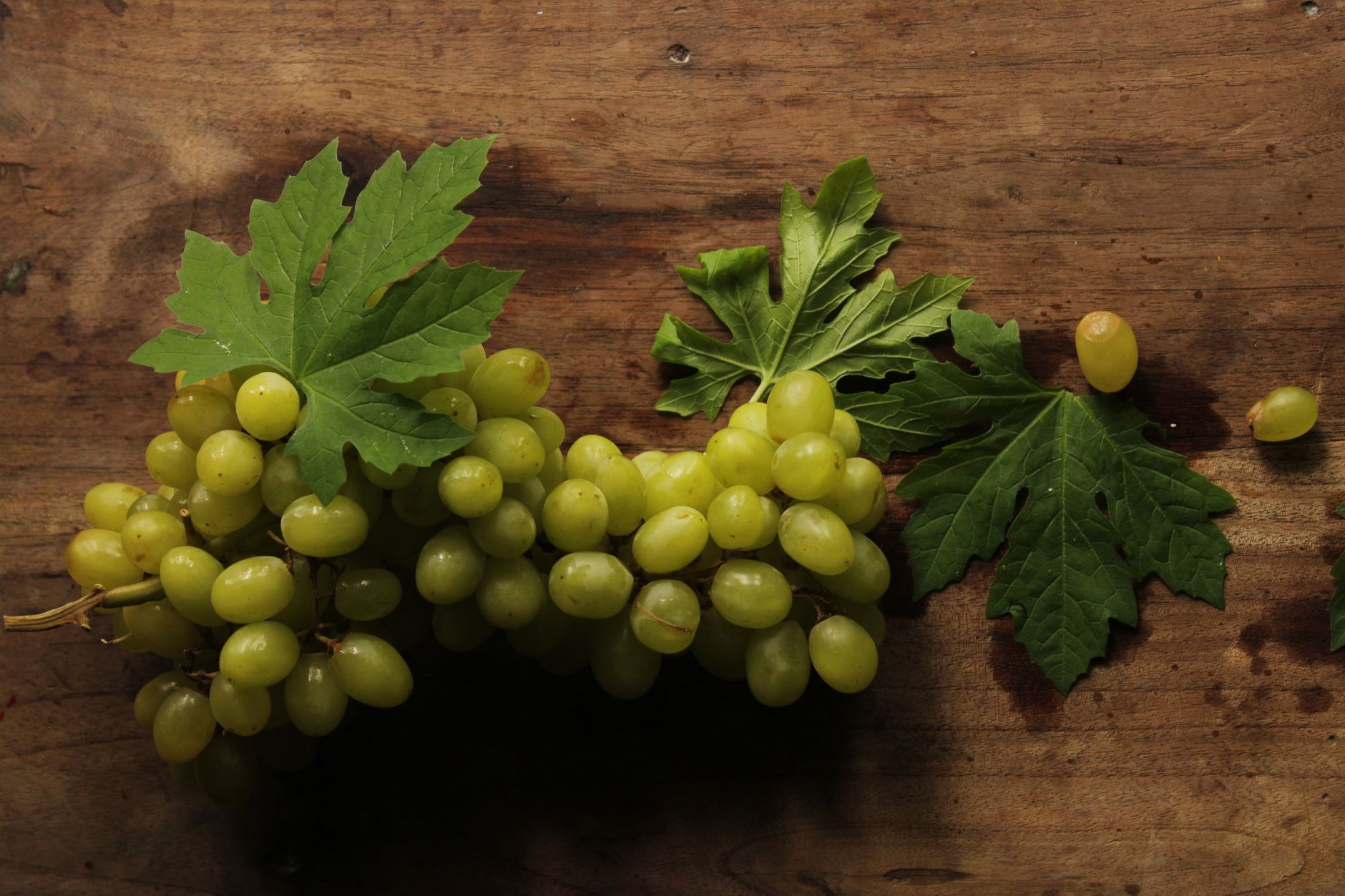 Bunch of fresh green grapes with leaves on a wooden table surface.