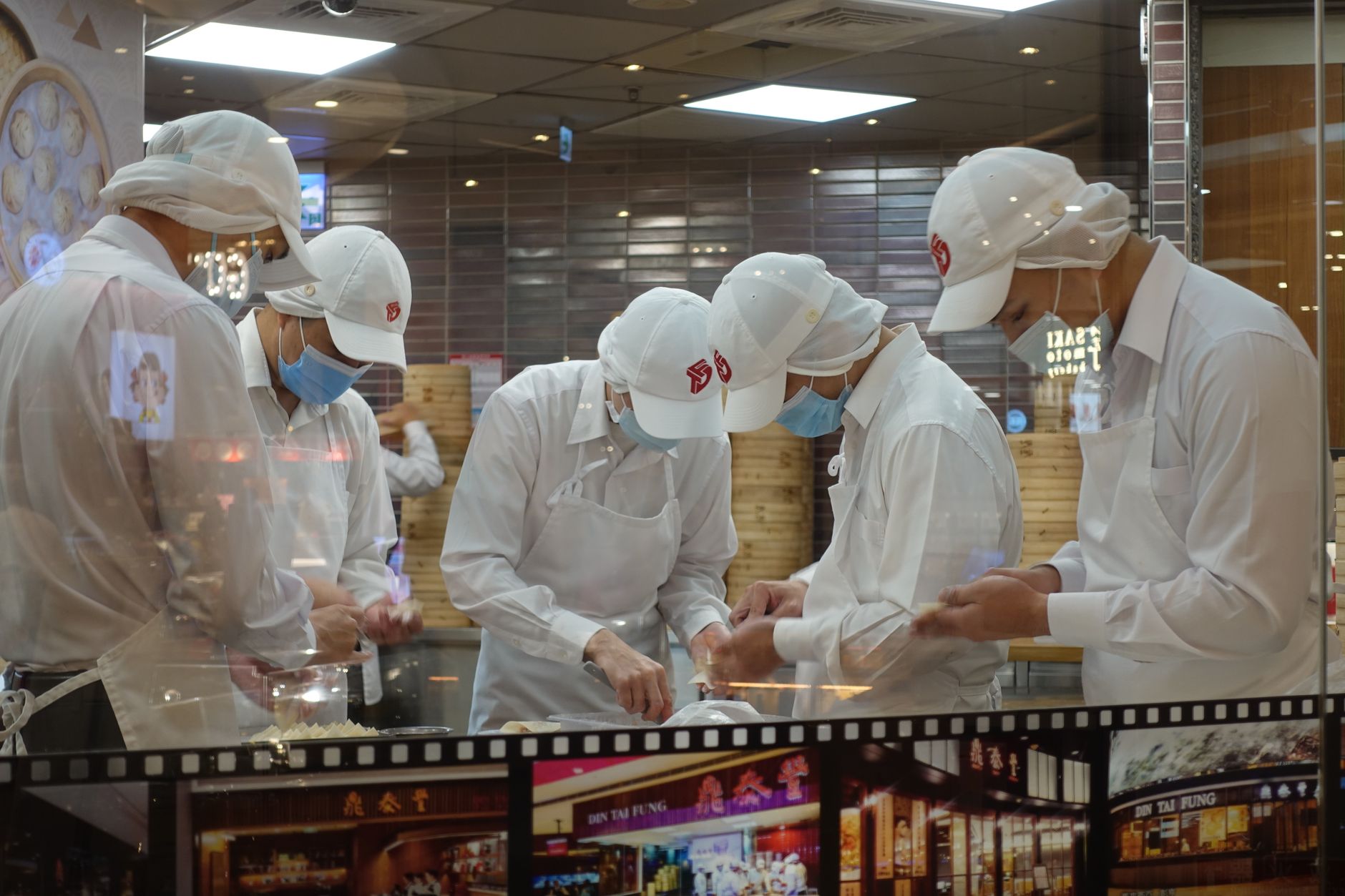 Five chefs wearing uniforms and masks diligently prepare dumplings in a Kaohsiung eatery.