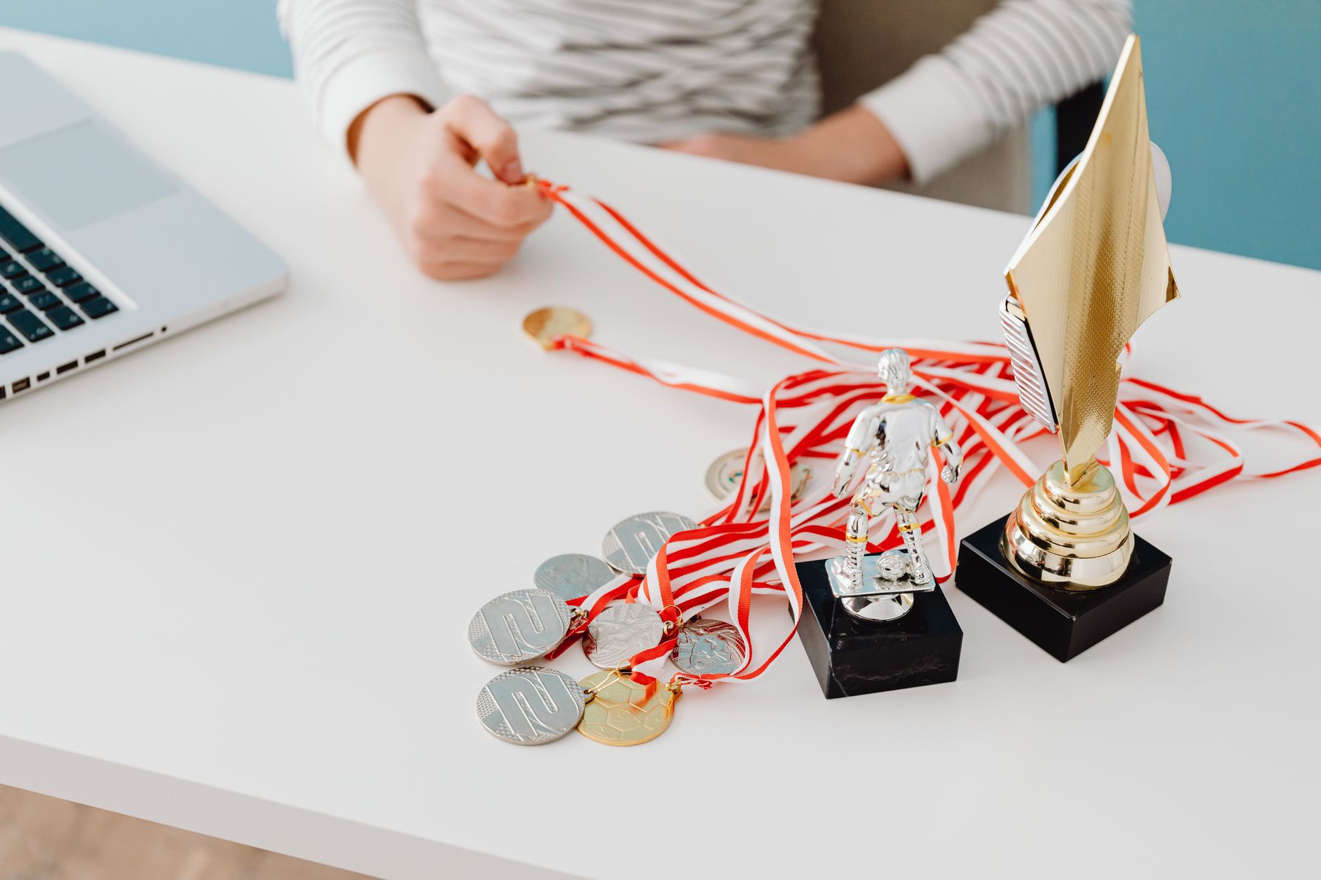 Young person displays football trophies and medals on a desk, showcasing athletic pride.
