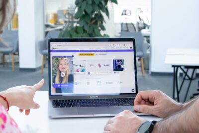 Two colleagues working together on a laptop screen in a modern office setting.