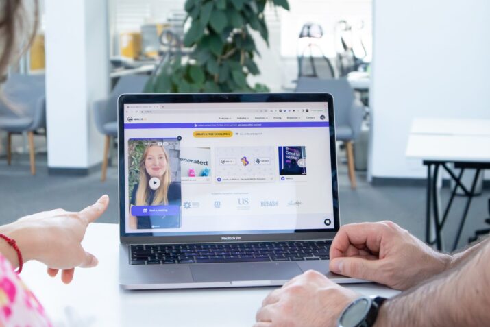 Two colleagues working together on a laptop screen in a modern office setting.