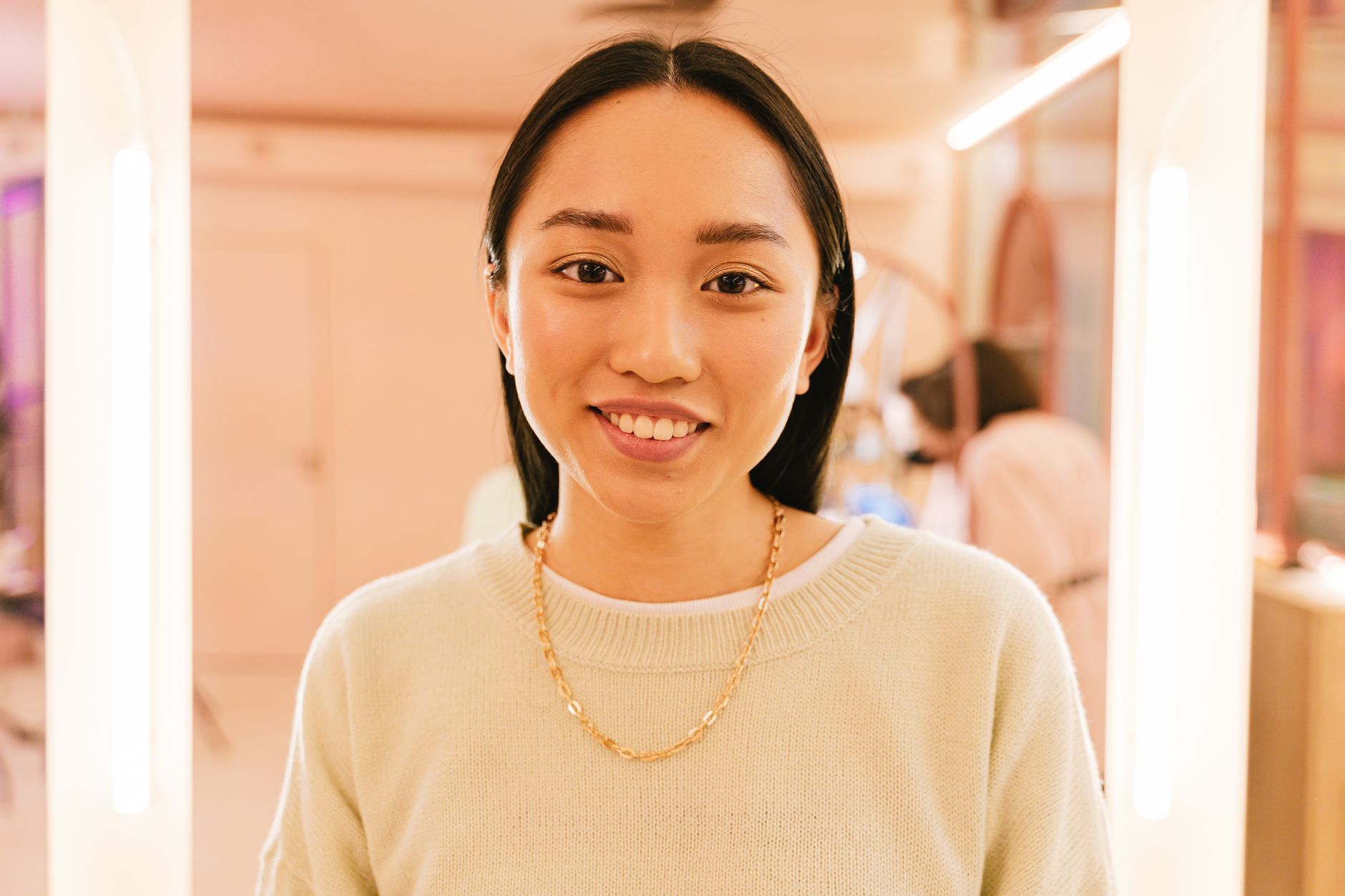 Close-up portrait of a smiling woman indoors with soft warm lighting.