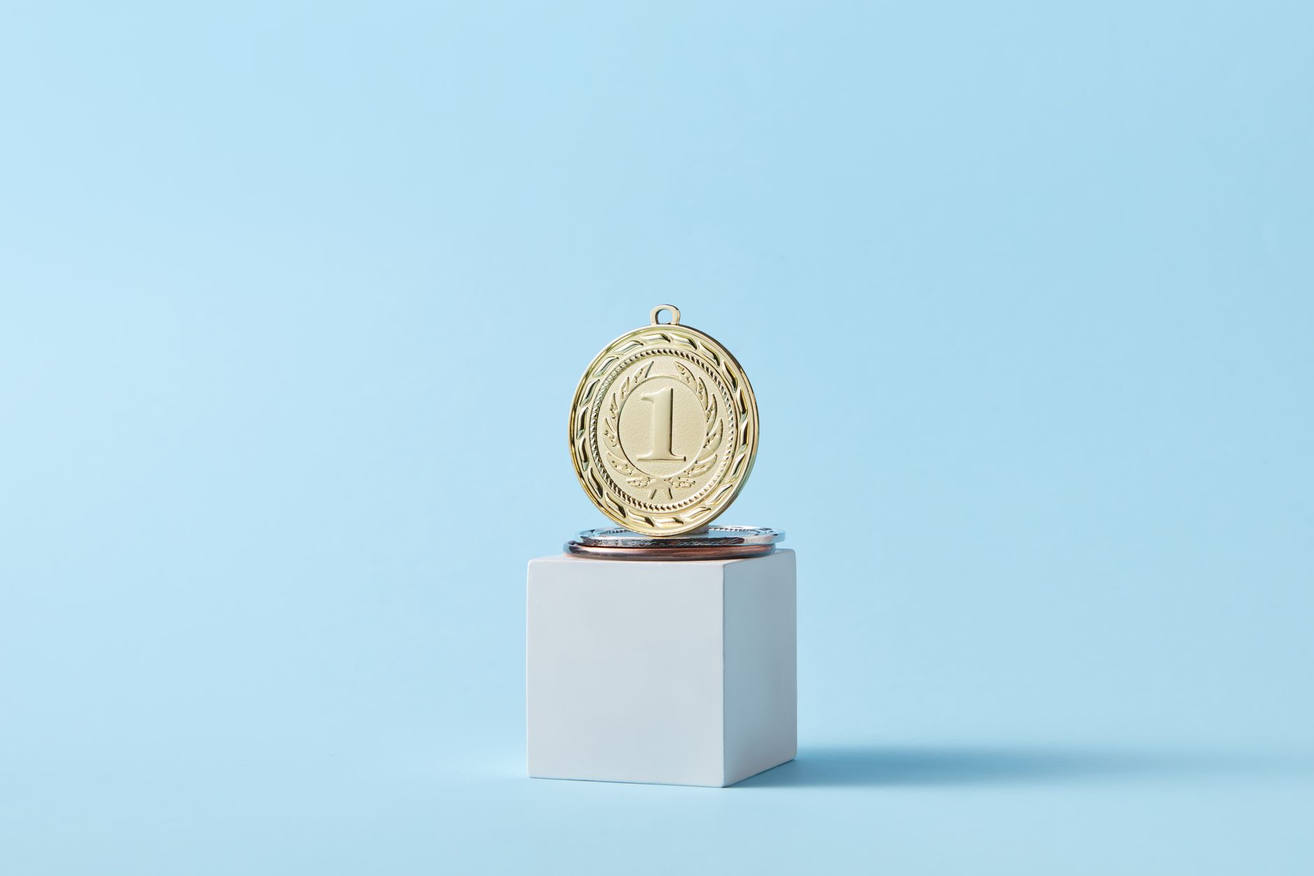 Close-up of a gold medal on a podium with a baby blue background, symbolizing victory.