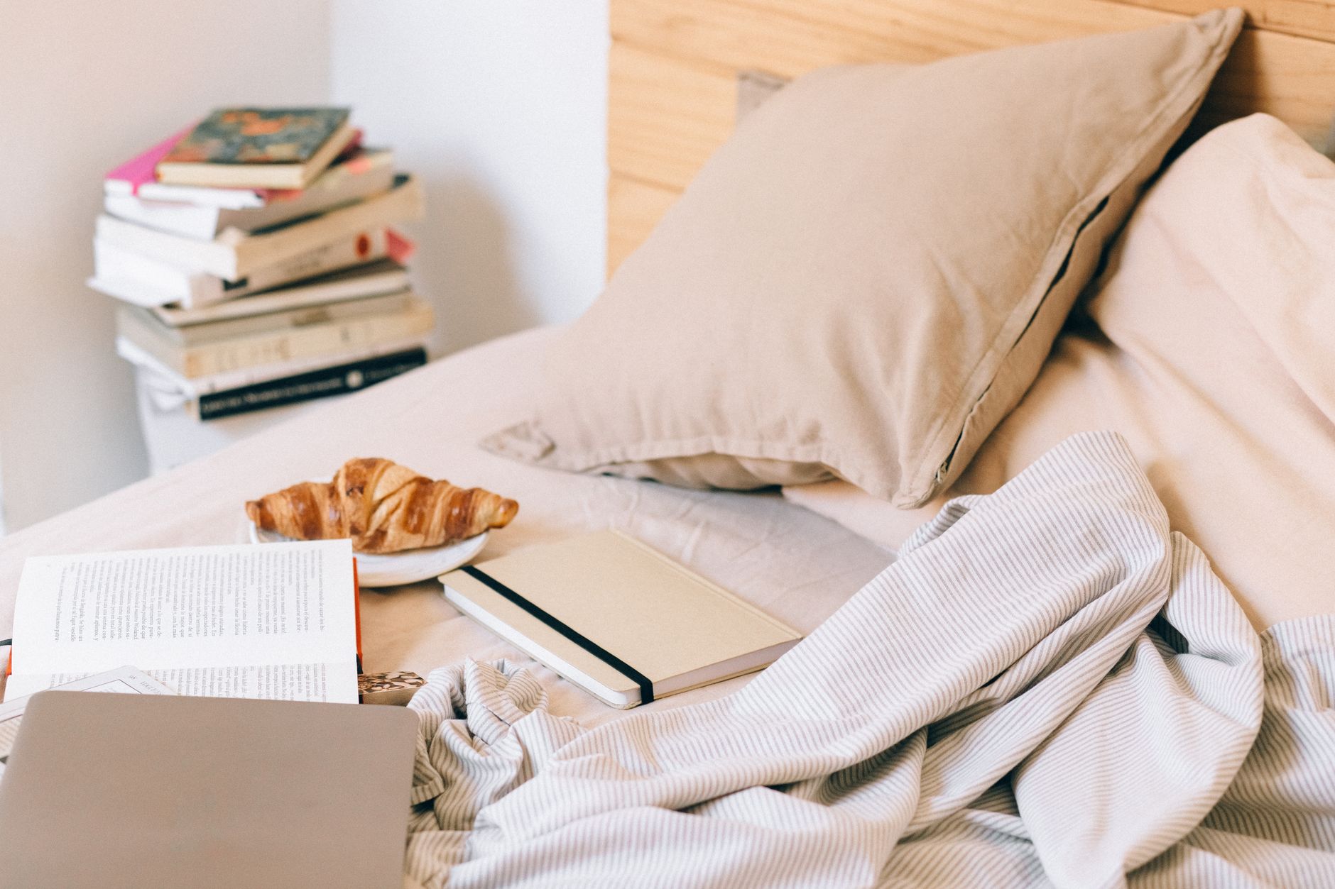 A cozy bed with a croissant, books, and a planner, creating a warm morning vibe.