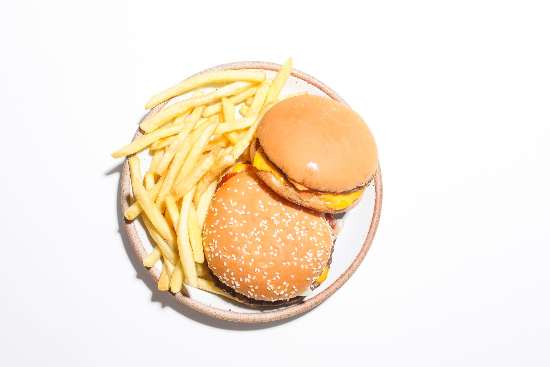 Two cheeseburgers and french fries served on a round plate against a white background.