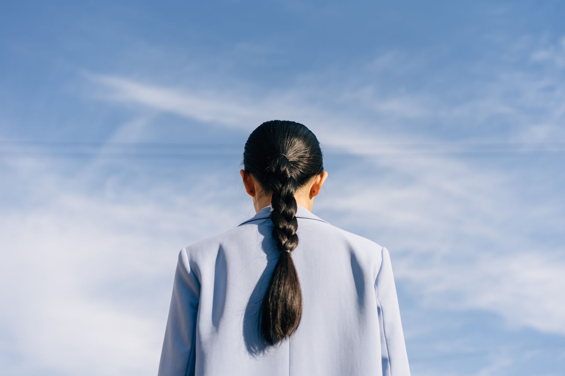 Back view of a woman with a braid against a vibrant blue sky. Ideal for concepts of freedom and aspiration.