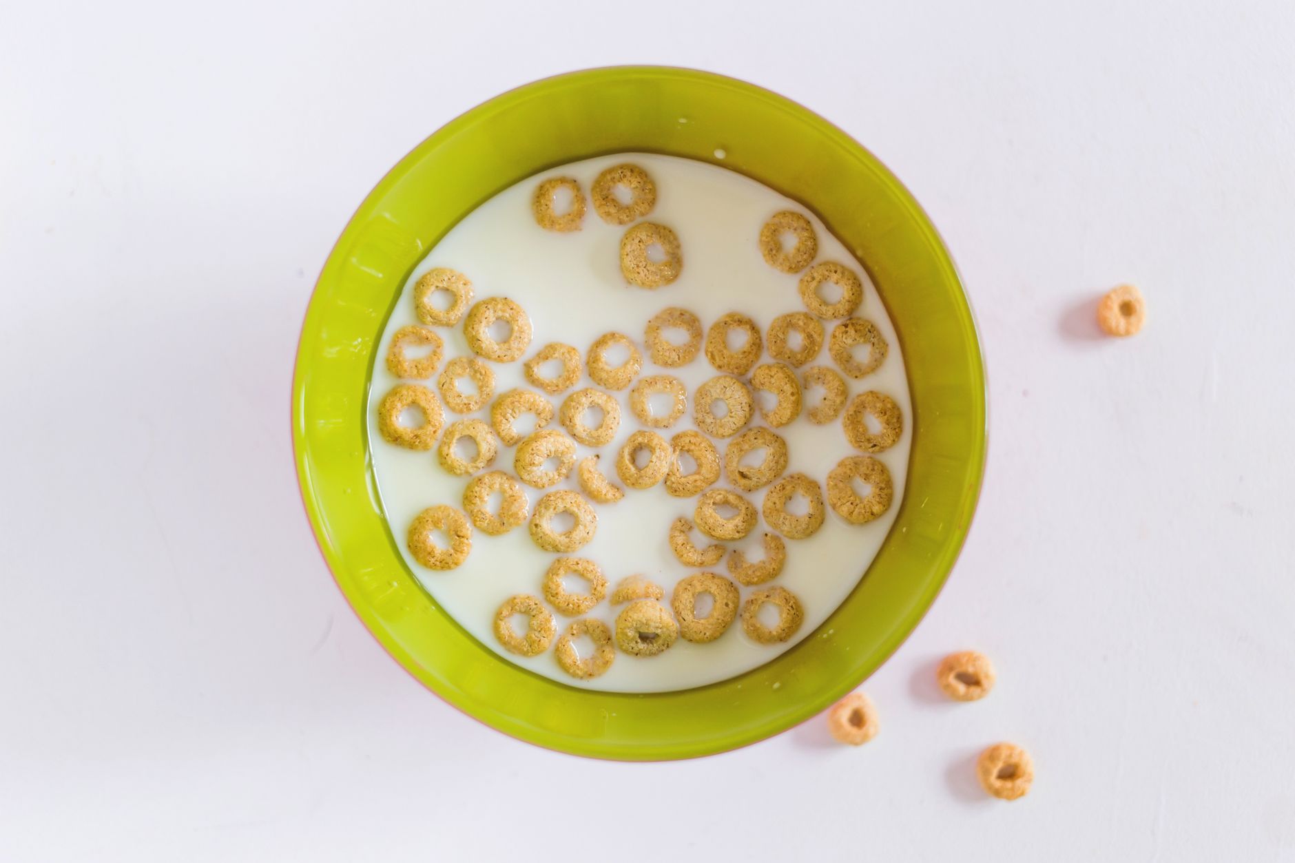 Top view of a green bowl filled with milk and cereal rings, ideal for a healthy breakfast.