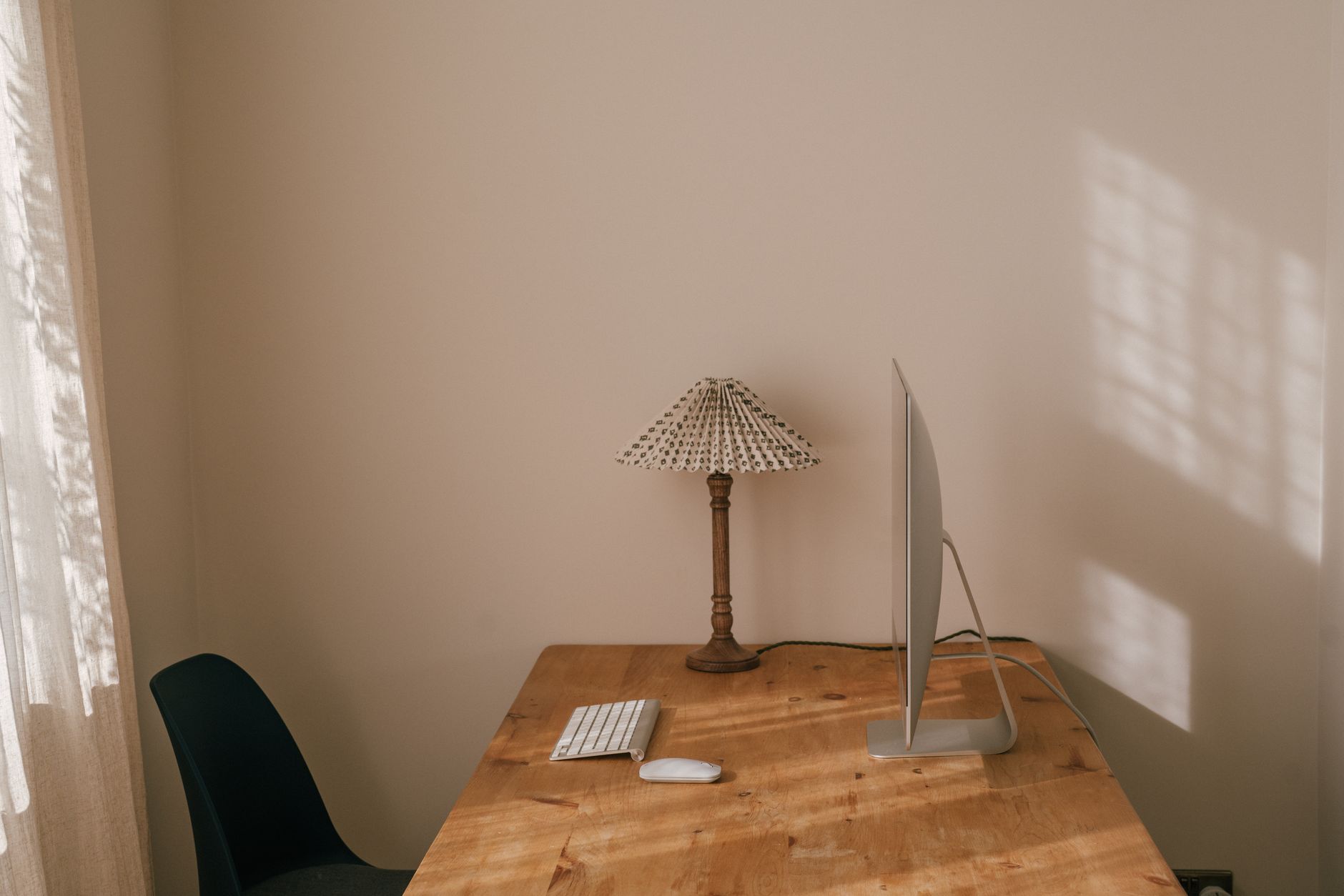 Simple home office desk with computer, lamp, and chair in natural daylight.