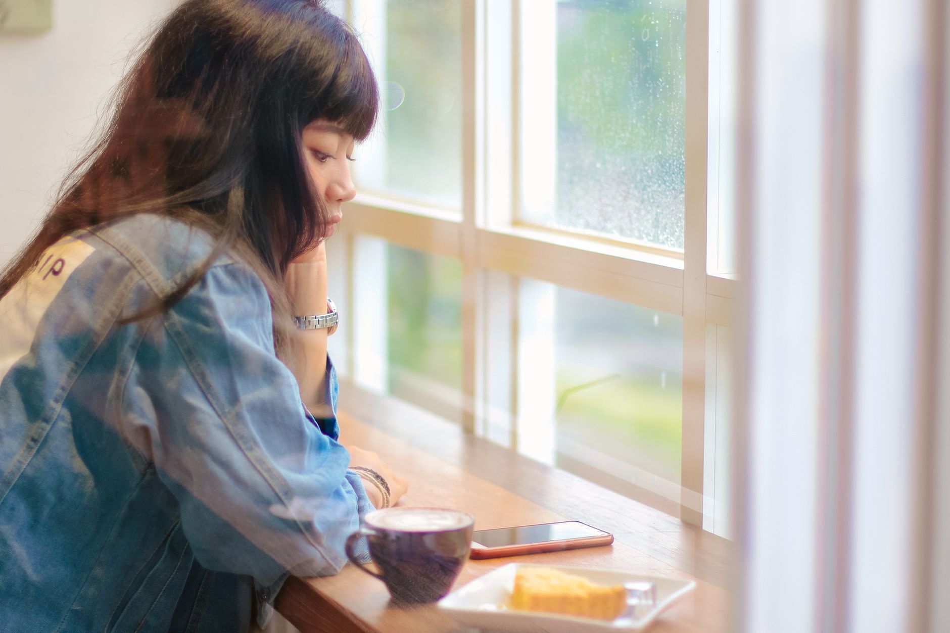 Young woman in a cafe sipping coffee and gazing outside a window, reflecting a serene moment.