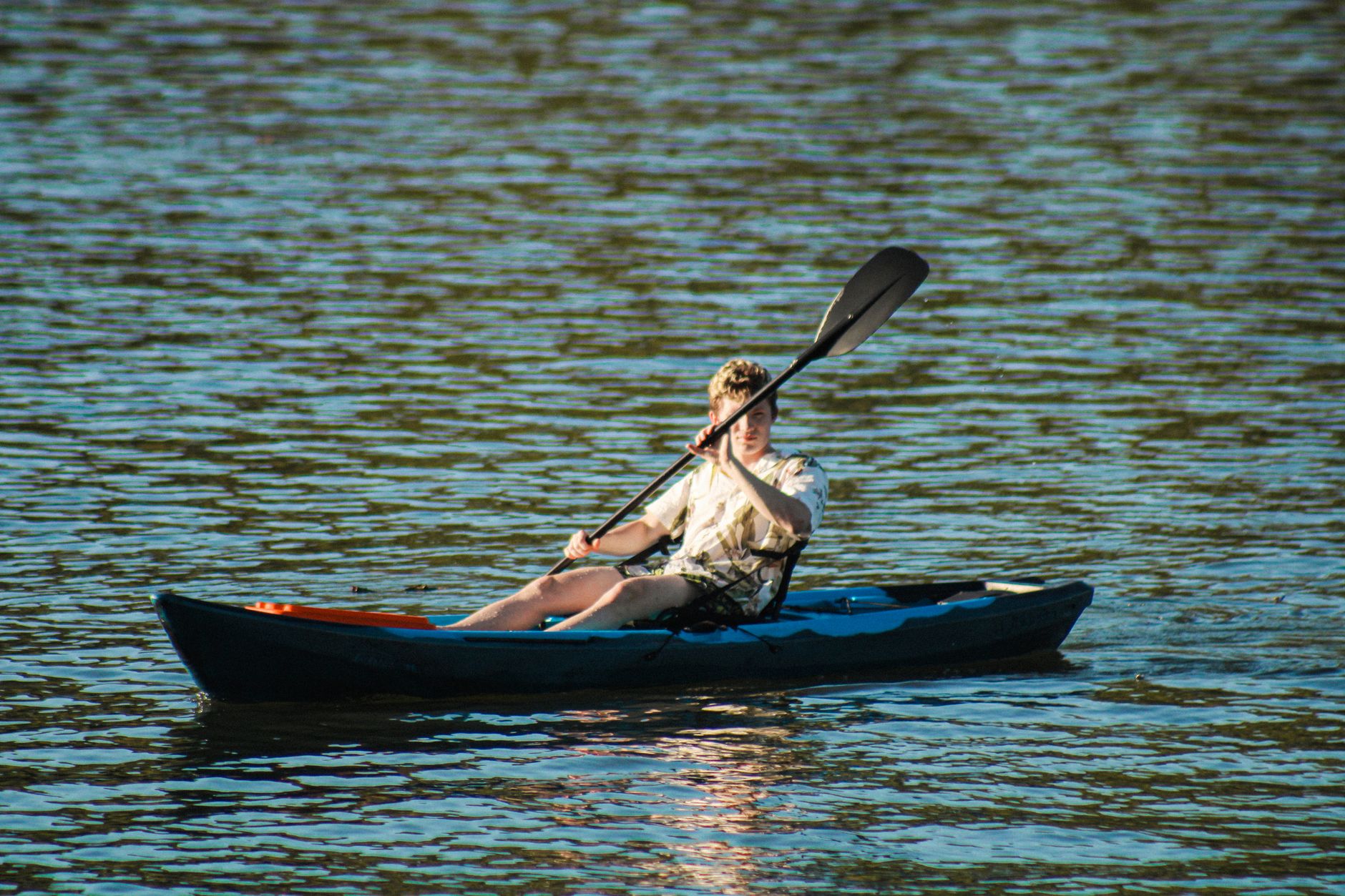 Adult male enjoying canoeing on a tranquil river under bright sunlight.