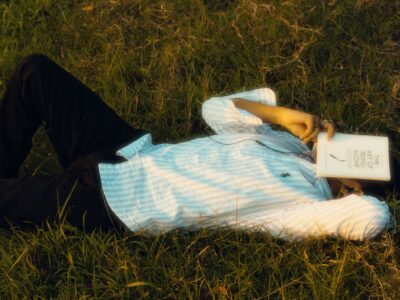 Person lying on grass with a book covering face, enjoying solitude.