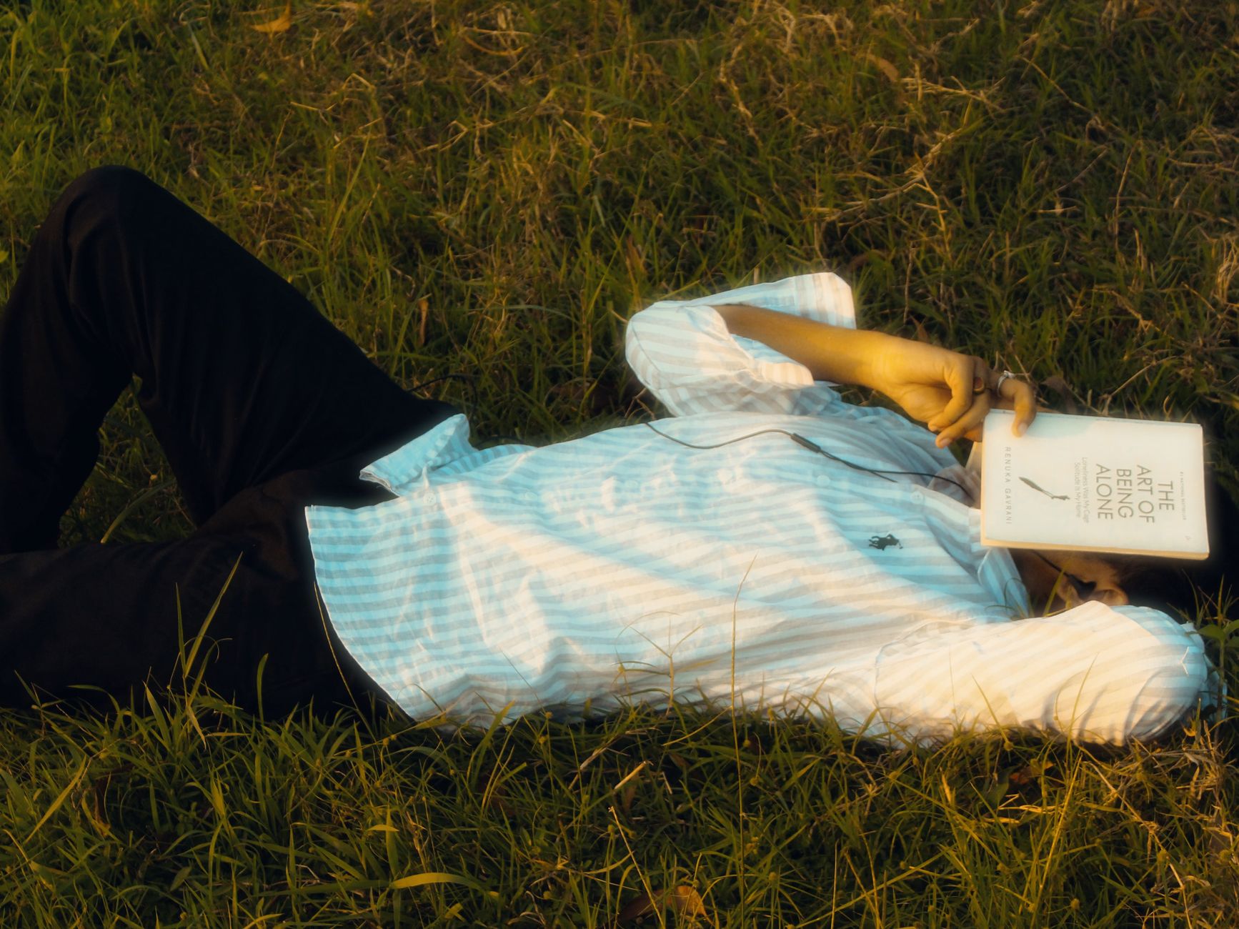 Person lying on grass with a book covering face, enjoying solitude.
