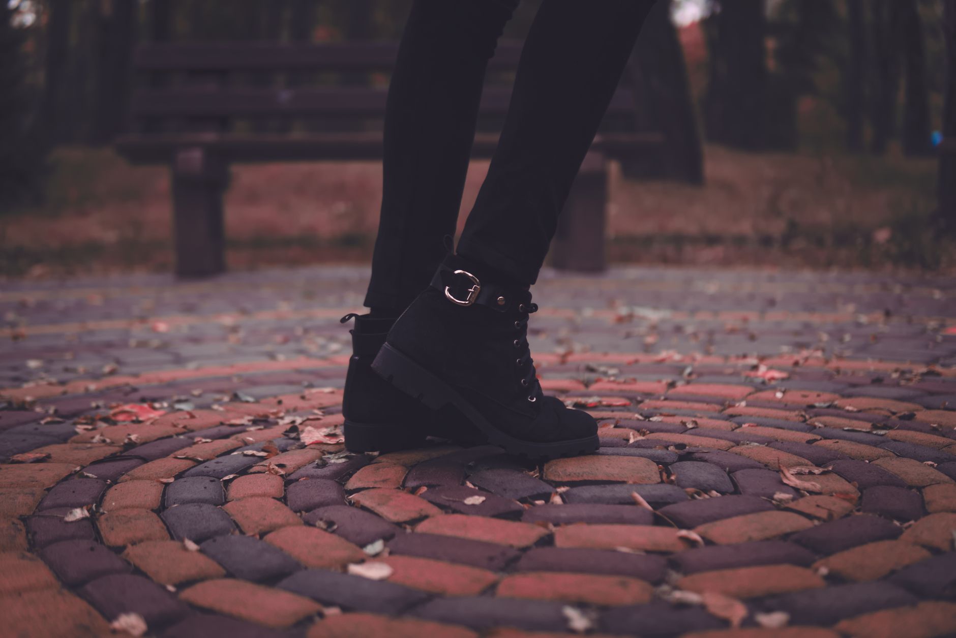 A stylish pair of black boots on a patterned stone walkway during fall.
